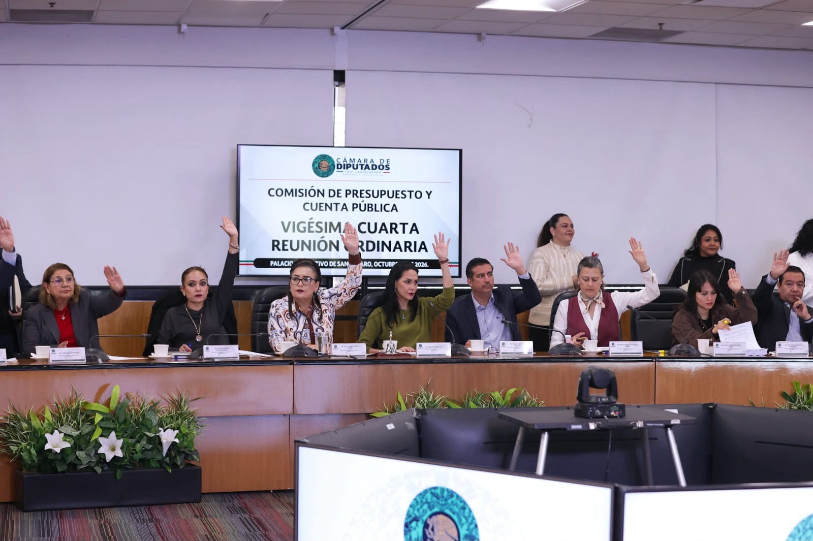 Integrantes de la Comisión de Presupuesto y Cuenta Pública levantan la mano para votar, sentados a la mesa de la sala de reuniones en San Lázaro.