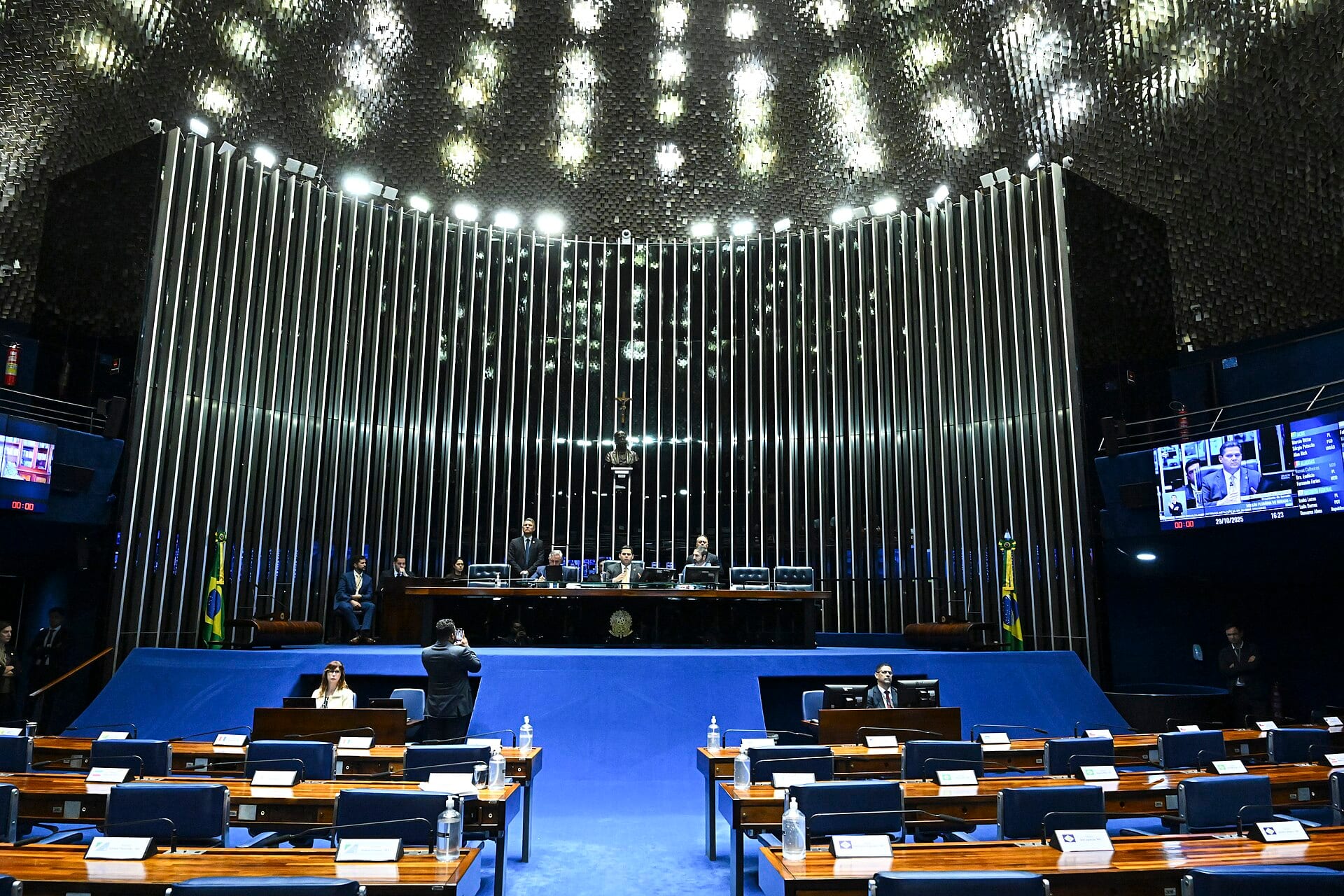 A wide view of Brazil's Senate chamber, with the presiding table in the background and empty blue seats in the foreground.