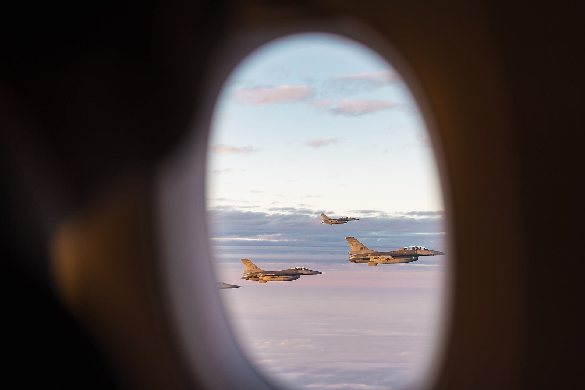 Tres cazas F-16 de la fuerza aérea taiwanesa vuelan en formación entre nubes al atardecer, vistos desde la ventanilla de un avión.