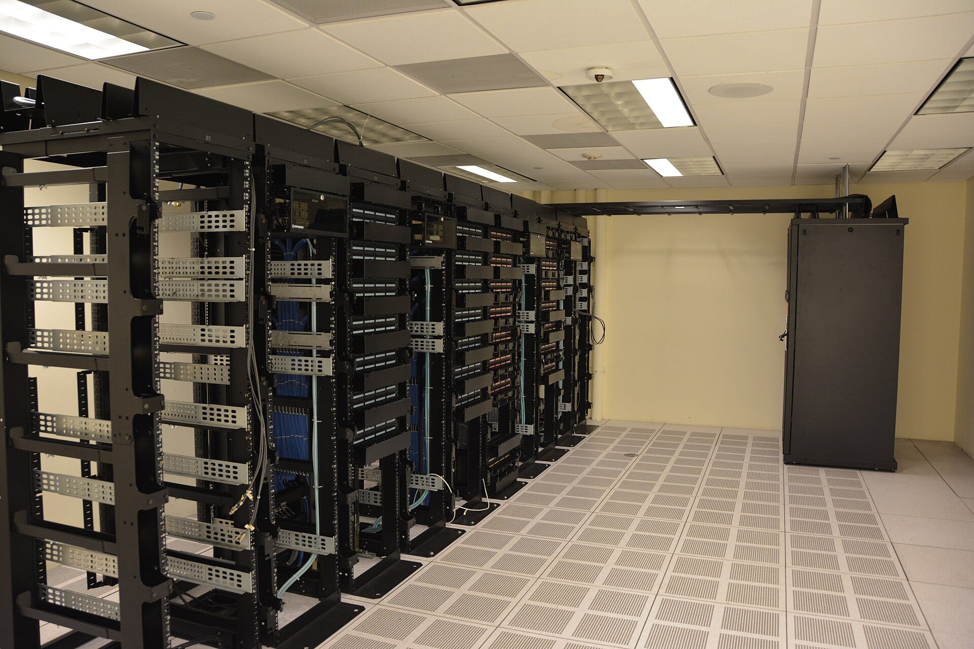 A server room with rows of black cabinets and a raised floor with perforated tiles.