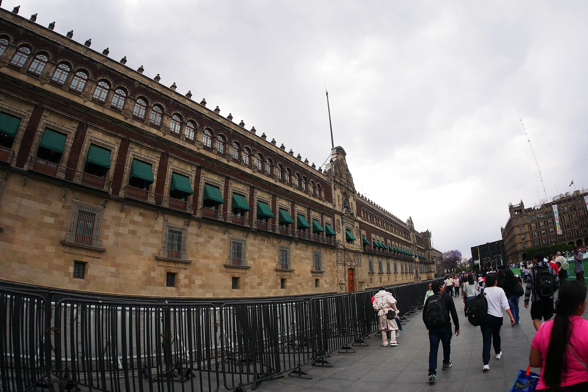 Un costado de Palacio Nacional con toldos verdes en los balcones y vallas metálicas al frente, mientras varias personas caminan por la plaza.