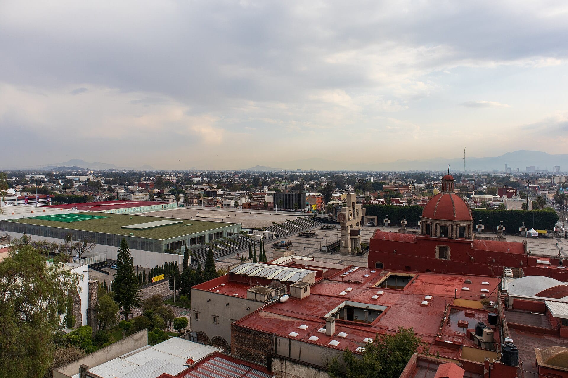 Vista aérea de Gustavo A. Madero con azoteas rojas, tinacos y la explanada de la Plaza Mariana al fondo.