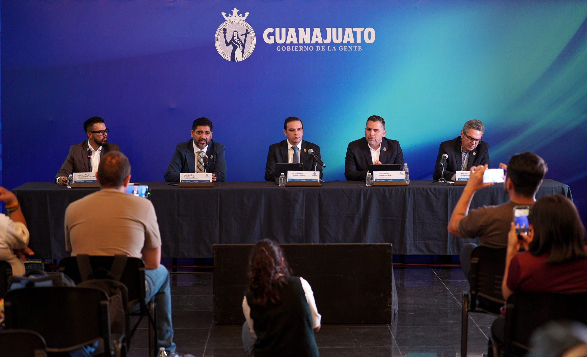 Cinco funcionarios del Gobierno de Guanajuato sentados tras una mesa, bajo un fondo azul con el logotipo del estado, ante periodistas.