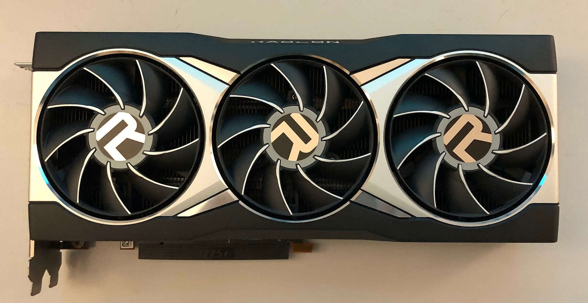 Vista frontal de una tarjeta gráfica Radeon RX 6900 XT con tres ventiladores y carcasa gris oscura y plateada.
