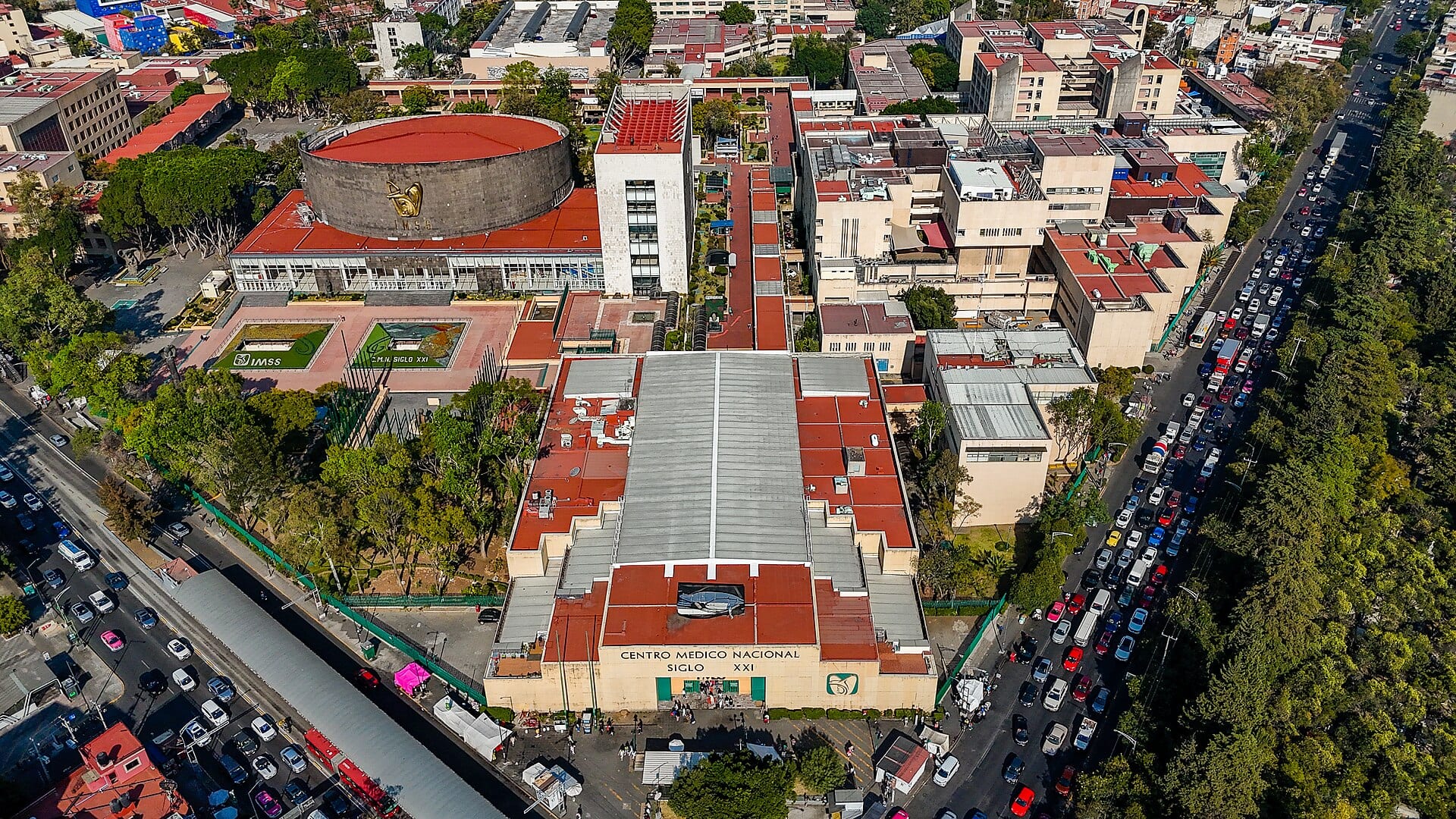 Vista aérea del Centro Médico Nacional Siglo XXI del IMSS, con sus edificios de techos rojos y una avenida con tráfico a un lado.