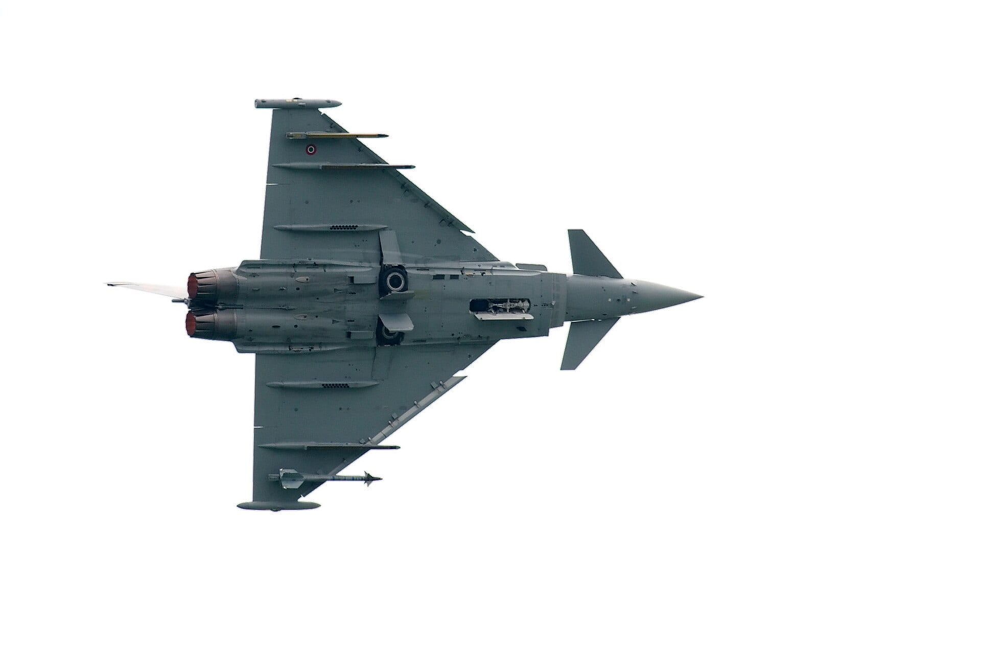 Un caza Eurofighter Typhoon de la fuerza aérea italiana, visto desde abajo y de perfil, sobre un cielo blanco.