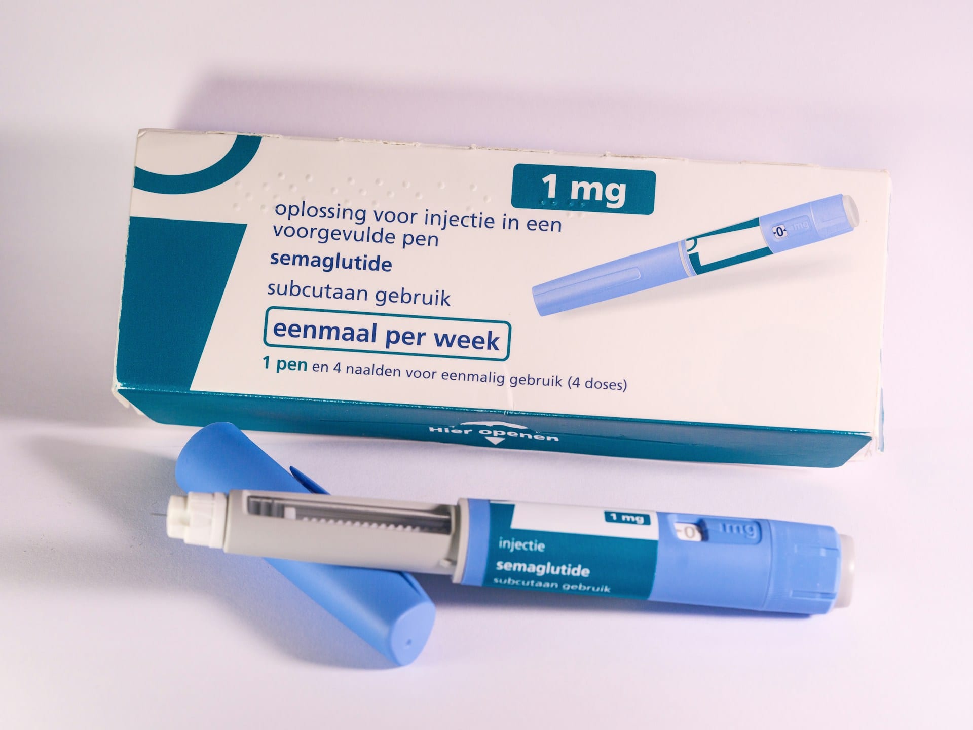 Una caja de medicamento y una pluma de inyección azul con la tapa quitada, sobre una superficie clara.