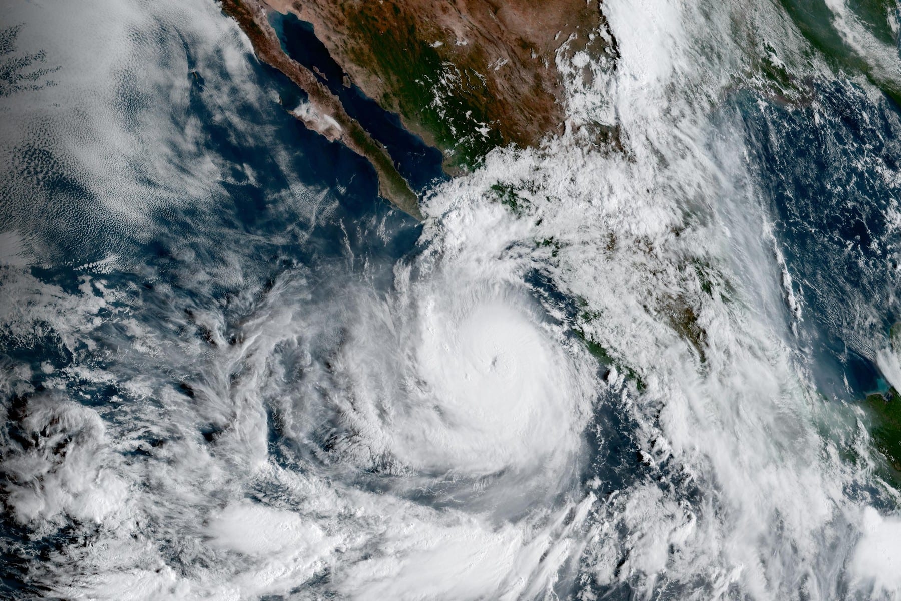 Imagen de satélite en color natural de un huracán con ojo definido frente a la costa del Pacífico mexicano, con la península de Baja California arriba a la izquierda.