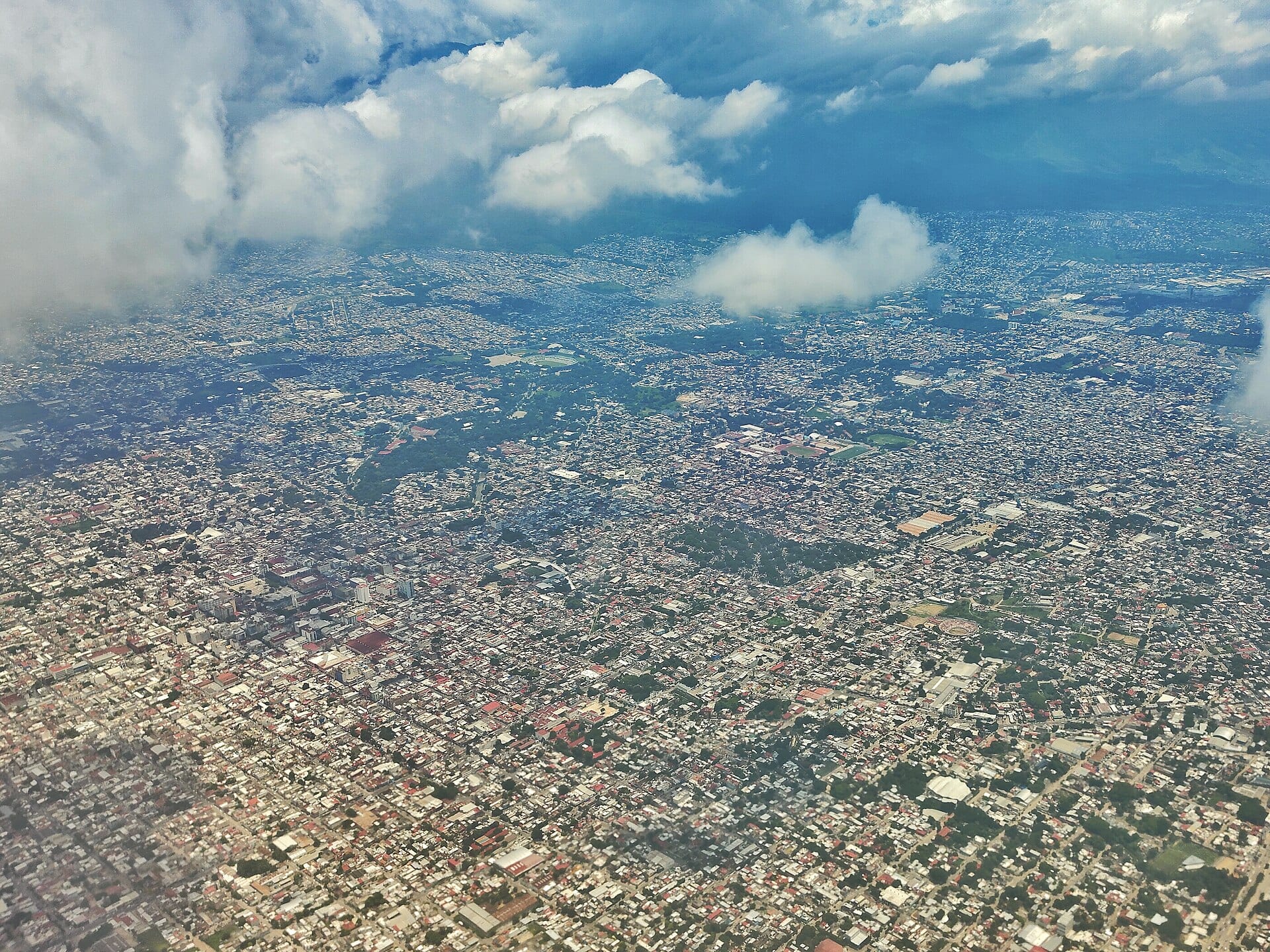 Vista aérea de Tuxtla Gutiérrez entre nubes, con manzanas de casas y áreas verdes que llegan hasta las montañas.