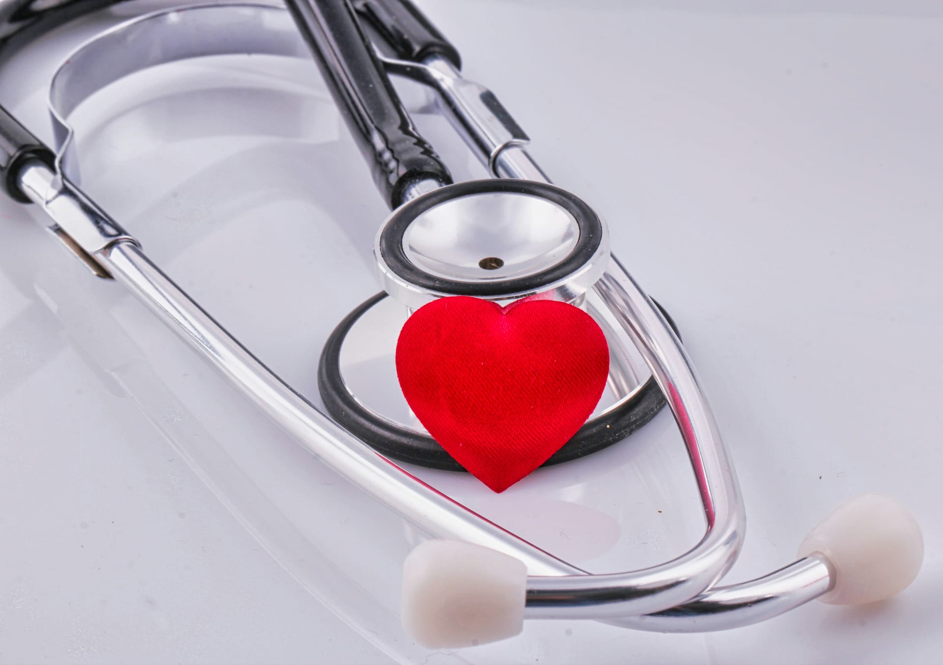Un estetoscopio plateado enrollado junto a un pequeño corazón de tela roja.