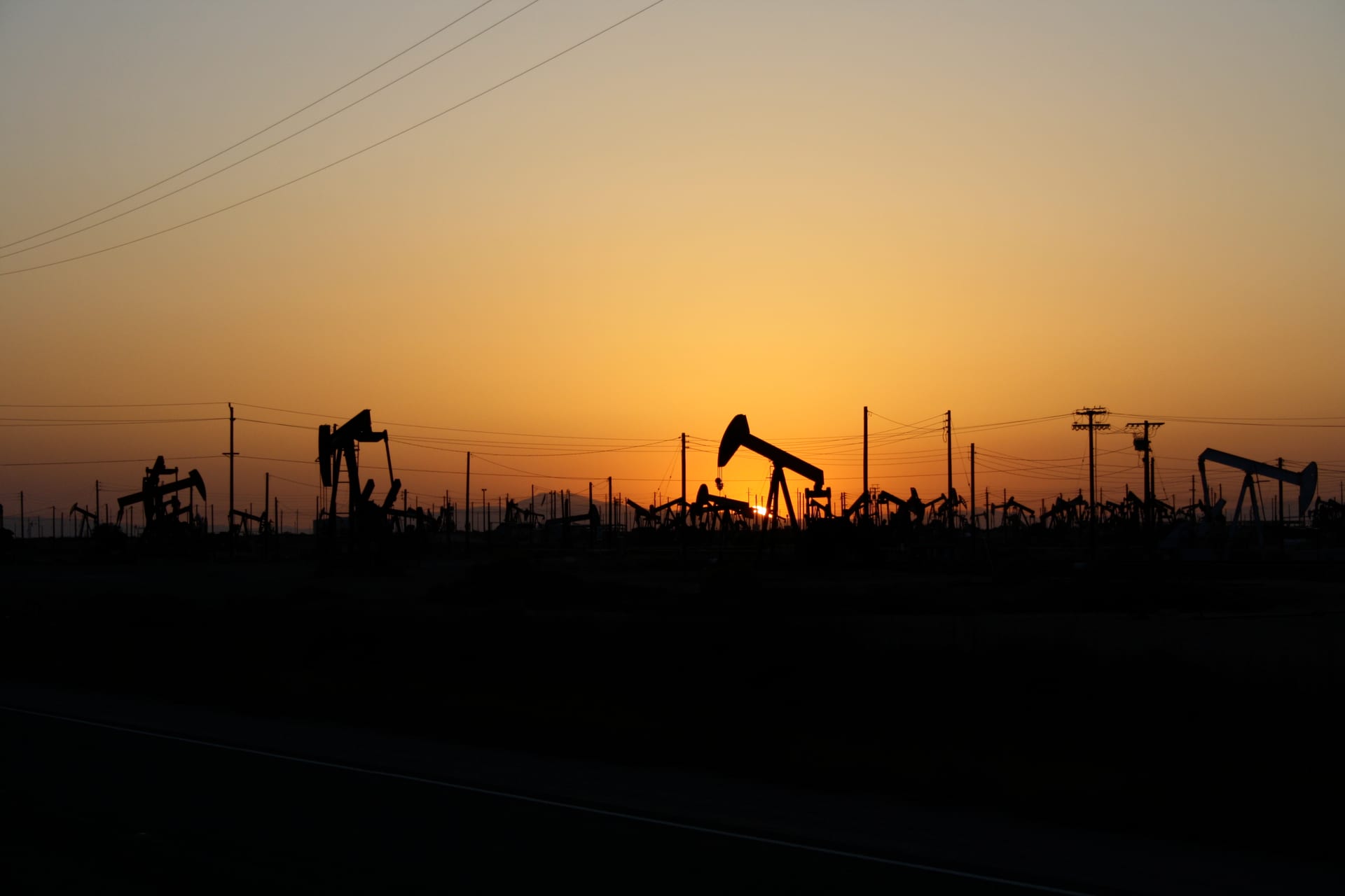 Silhouetted oil pumpjacks against an orange sunset sky.