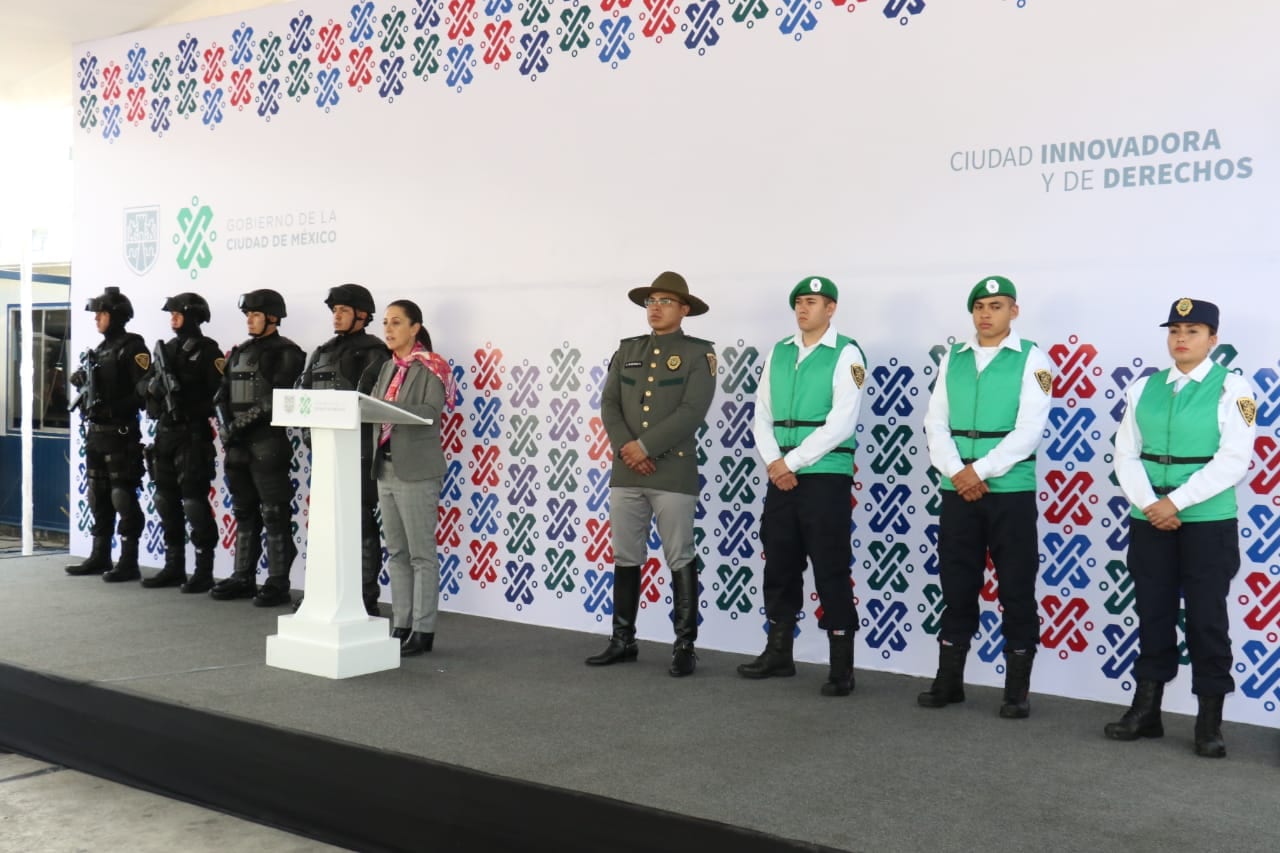 Una mujer habla en un podio junto a policías con equipo táctico y chalecos verdes, frente a una lona del Gobierno de la Ciudad de México.
