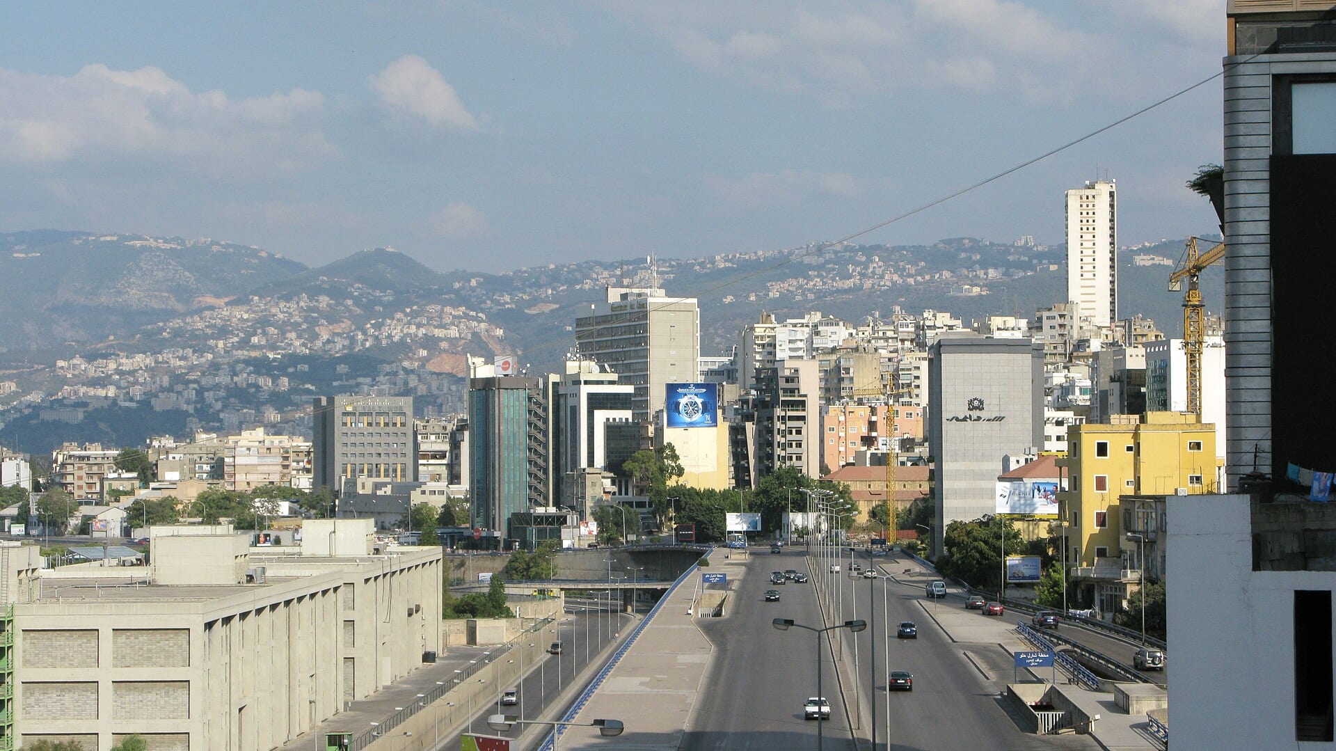 A nearly empty highway crosses Beirut, with office buildings and the hills along the coast in the background.