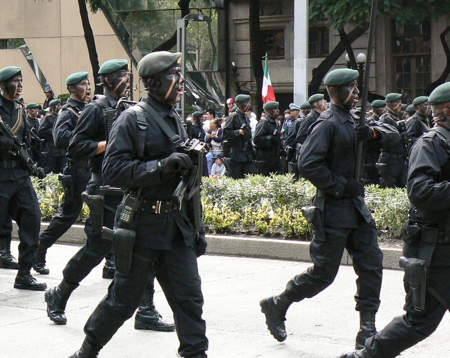 Un grupo de soldados con boina verde y el rostro pintado marcha en formación por una avenida, con fusiles y equipo táctico.