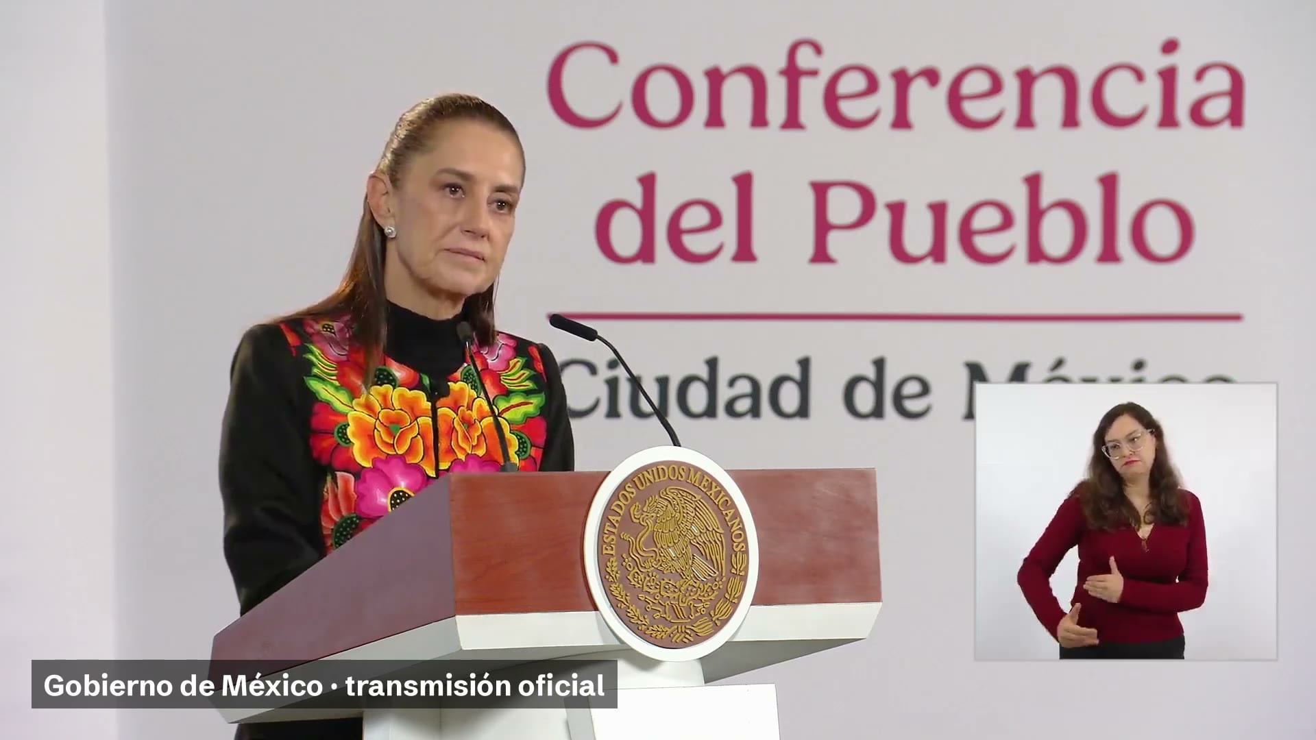 La presidenta Claudia Sheinbaum habla frente a un atril con el escudo nacional, bajo el letrero Conferencia del Pueblo; a la derecha, una intérprete de lengua de señas