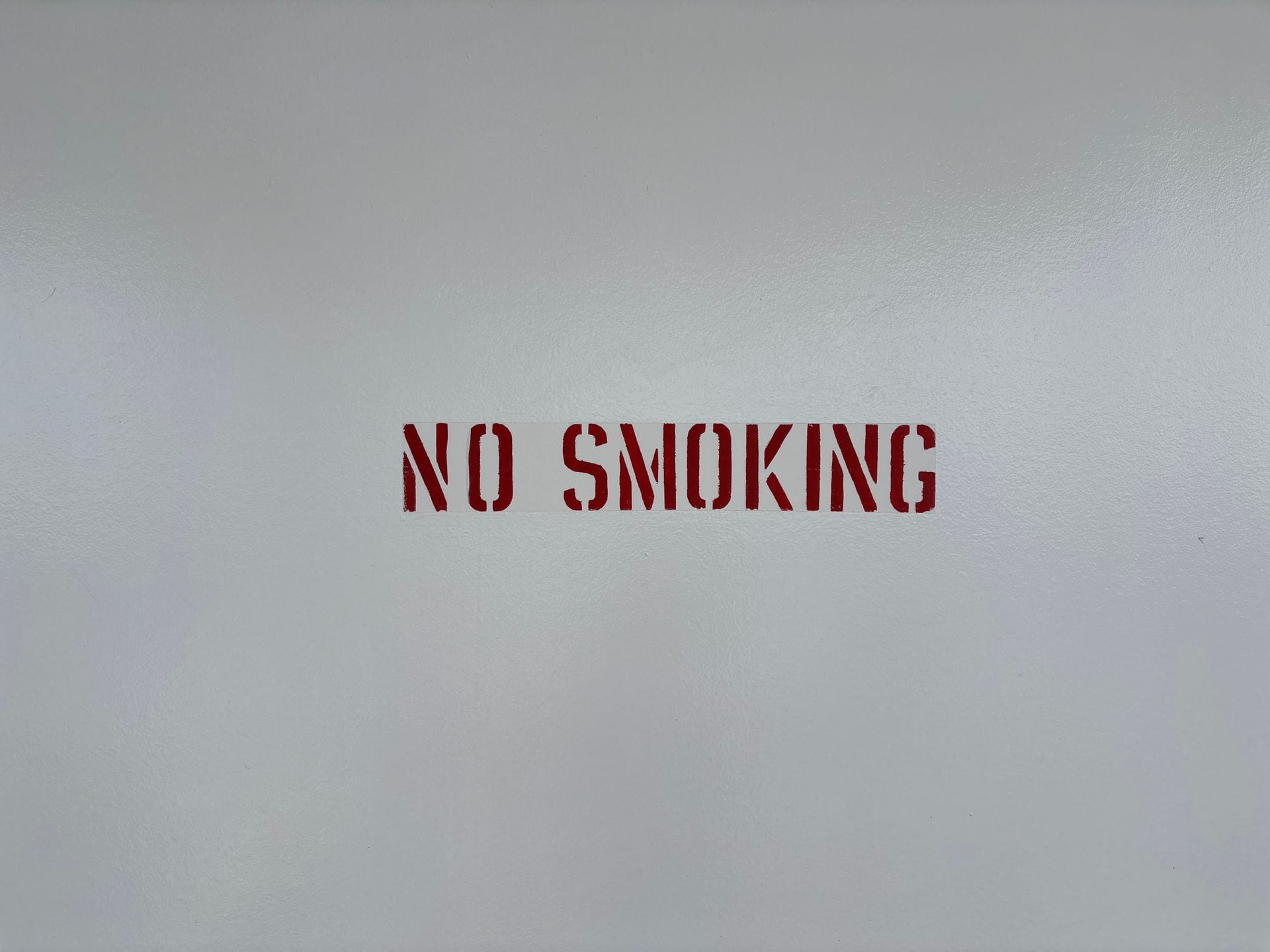 Letras rojas con la leyenda NO SMOKING pintadas con plantilla sobre una pared blanca.