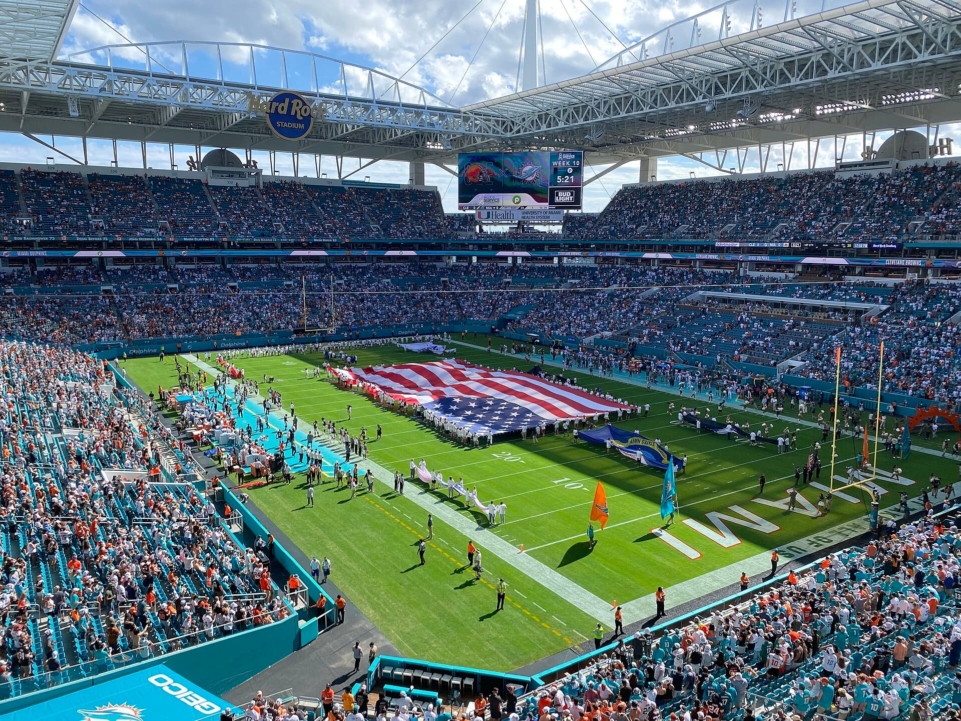 Vista general del Hard Rock Stadium de Miami durante el himno, con una bandera estadounidense gigante extendida sobre el césped y las gradas llenas.