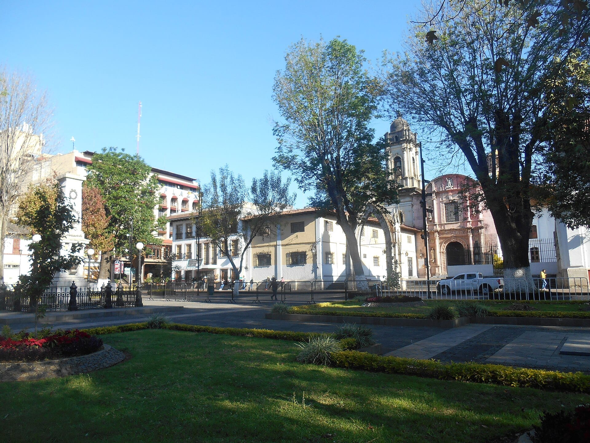 Jardines y edificios de la plaza del centro histórico de Uruapan, con un templo de torre de cantera al fondo.