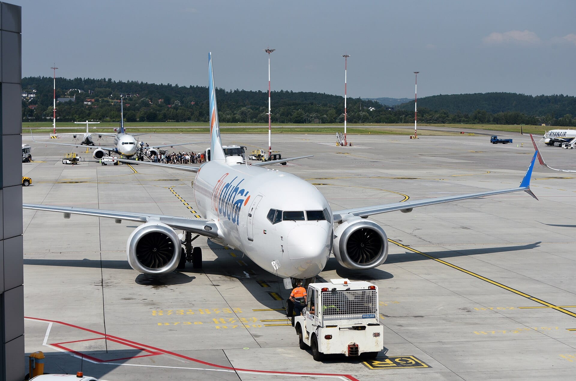 Un Boeing 737 blanco con el logotipo de Flydubai avanza remolcado en una plataforma de aeropuerto, con otros aviones al fondo.