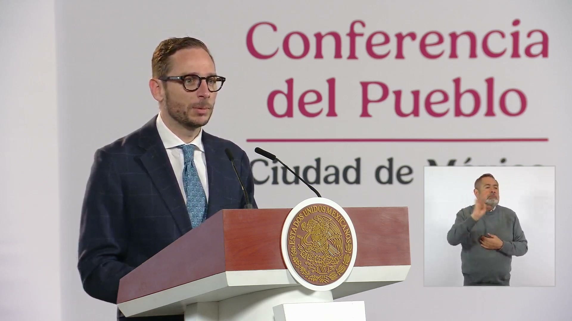 Eduardo Clark habla en el podio de la conferencia matutina, con un intérprete de lengua de señas a la derecha.