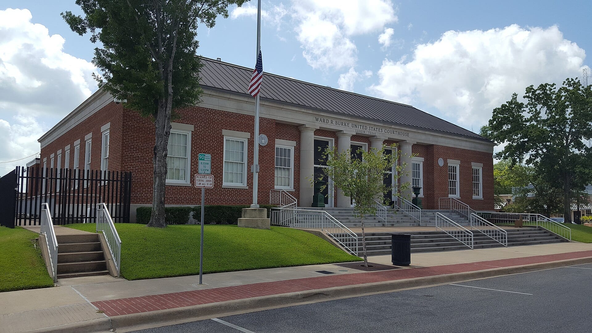 Red brick facade of the Ward R. Burke federal courthouse in Lufkin, Texas, with a U.S. flag in front of the entrance.