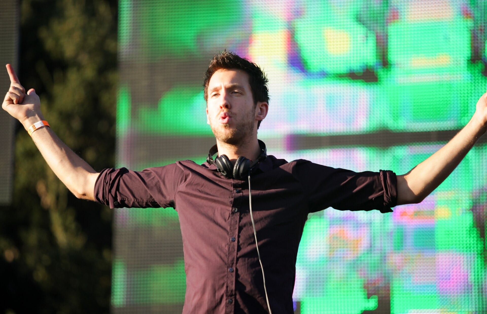El DJ Calvin Harris, con audífonos al cuello y los brazos abiertos, frente a una pantalla de colores durante una presentación en 2011.