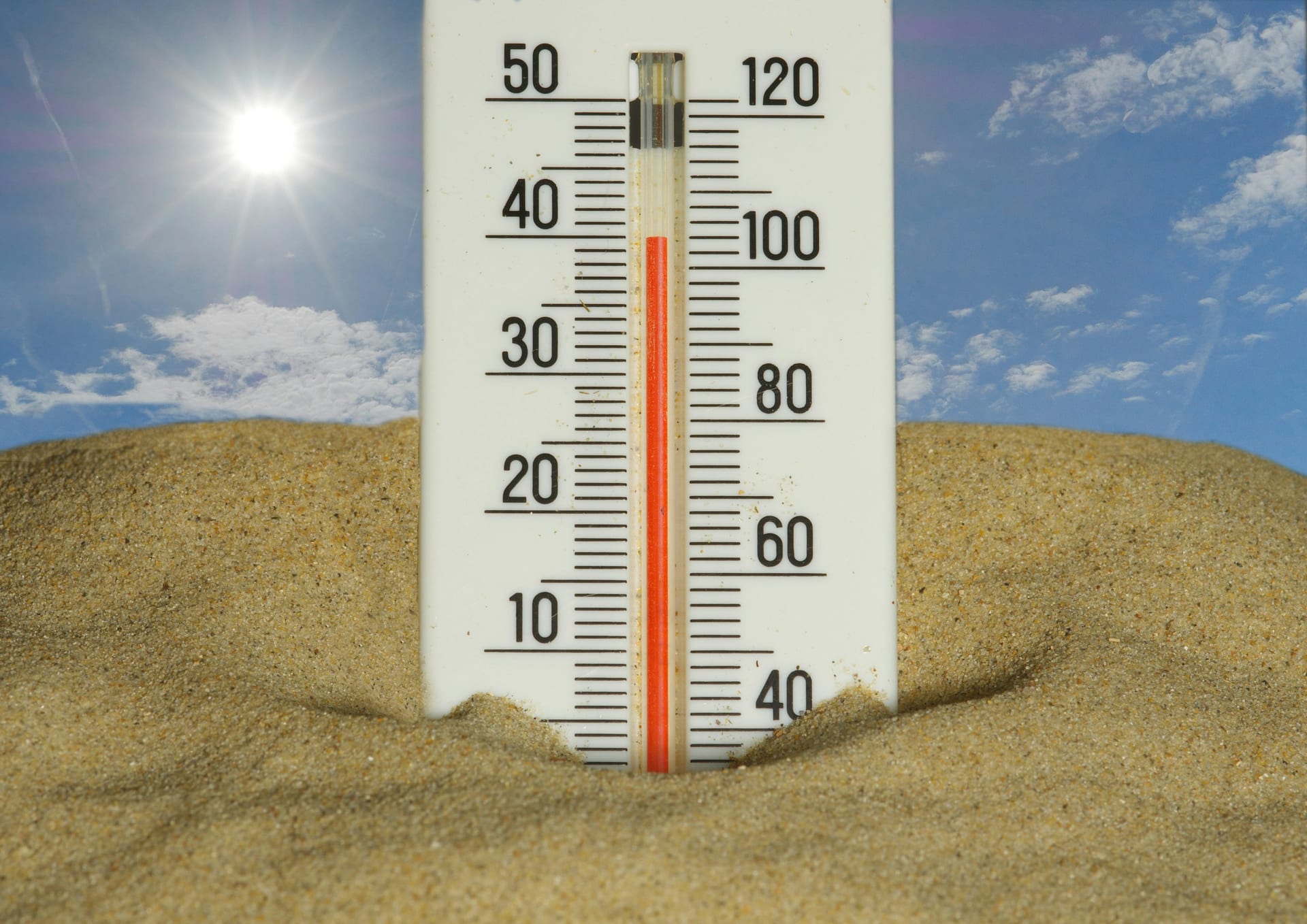 Un termómetro de pared clavado en la arena marca más de 35 grados bajo un sol intenso y un cielo azul.