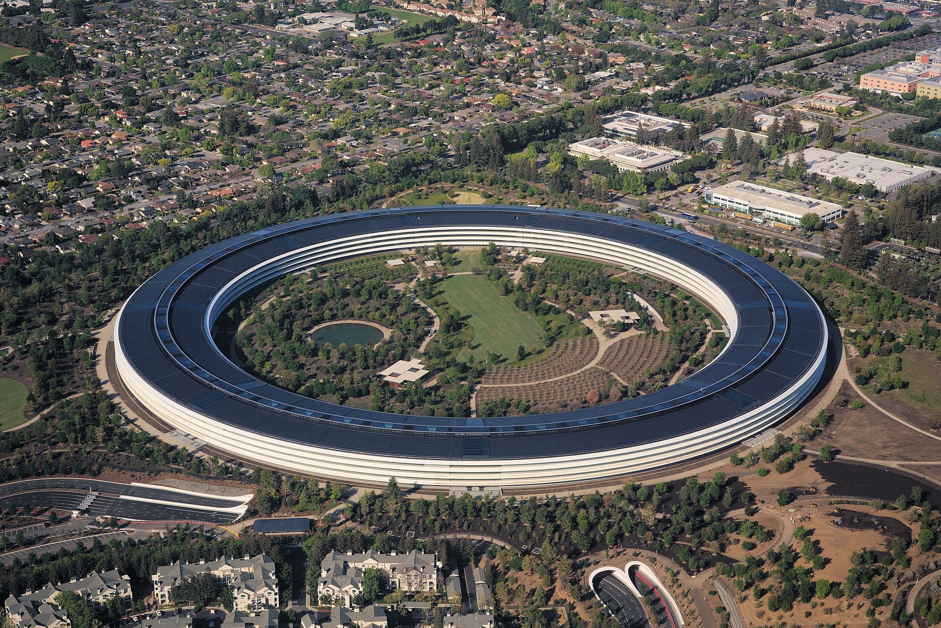 Vista aérea del edificio circular de Apple Park, rodeado de árboles y calles de Cupertino.