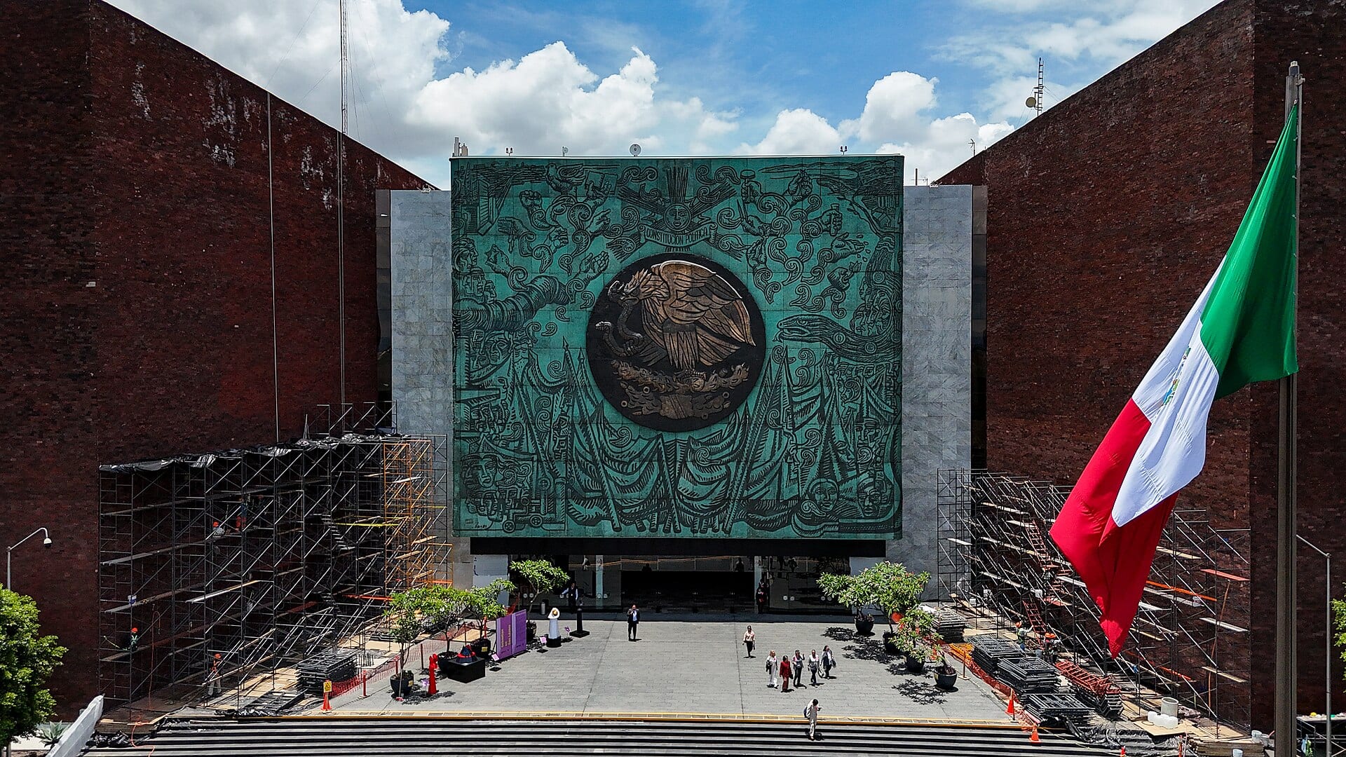 Fachada del Palacio Legislativo de San Lázaro vista desde arriba, con el mural de bronce y el águila entre dos muros de ladrillo y una bandera a la derecha.