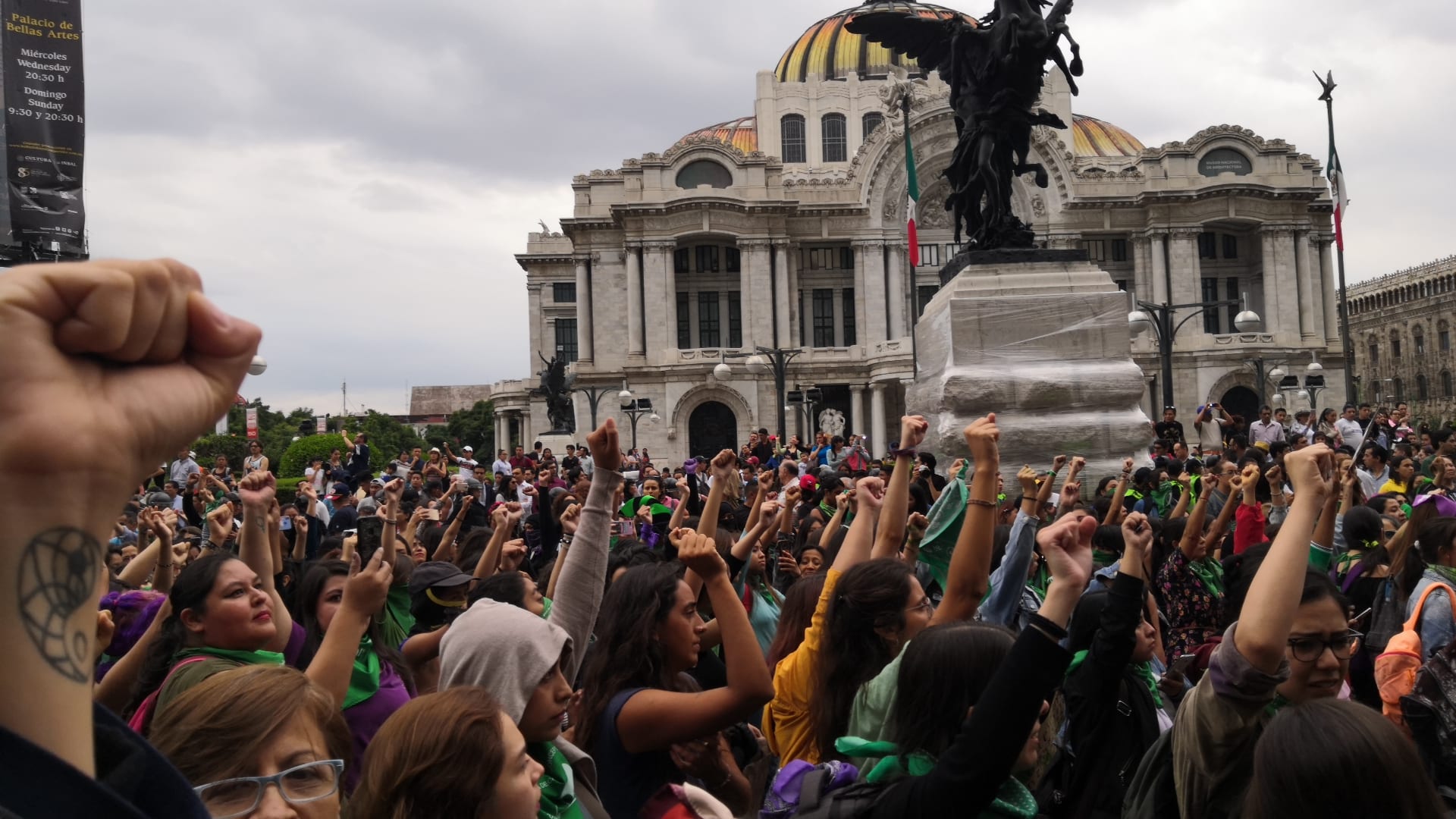 Un grupo de mujeres levanta el puño con pañuelos verdes y morados frente al Palacio de Bellas Artes durante una marcha por el derecho al aborto.