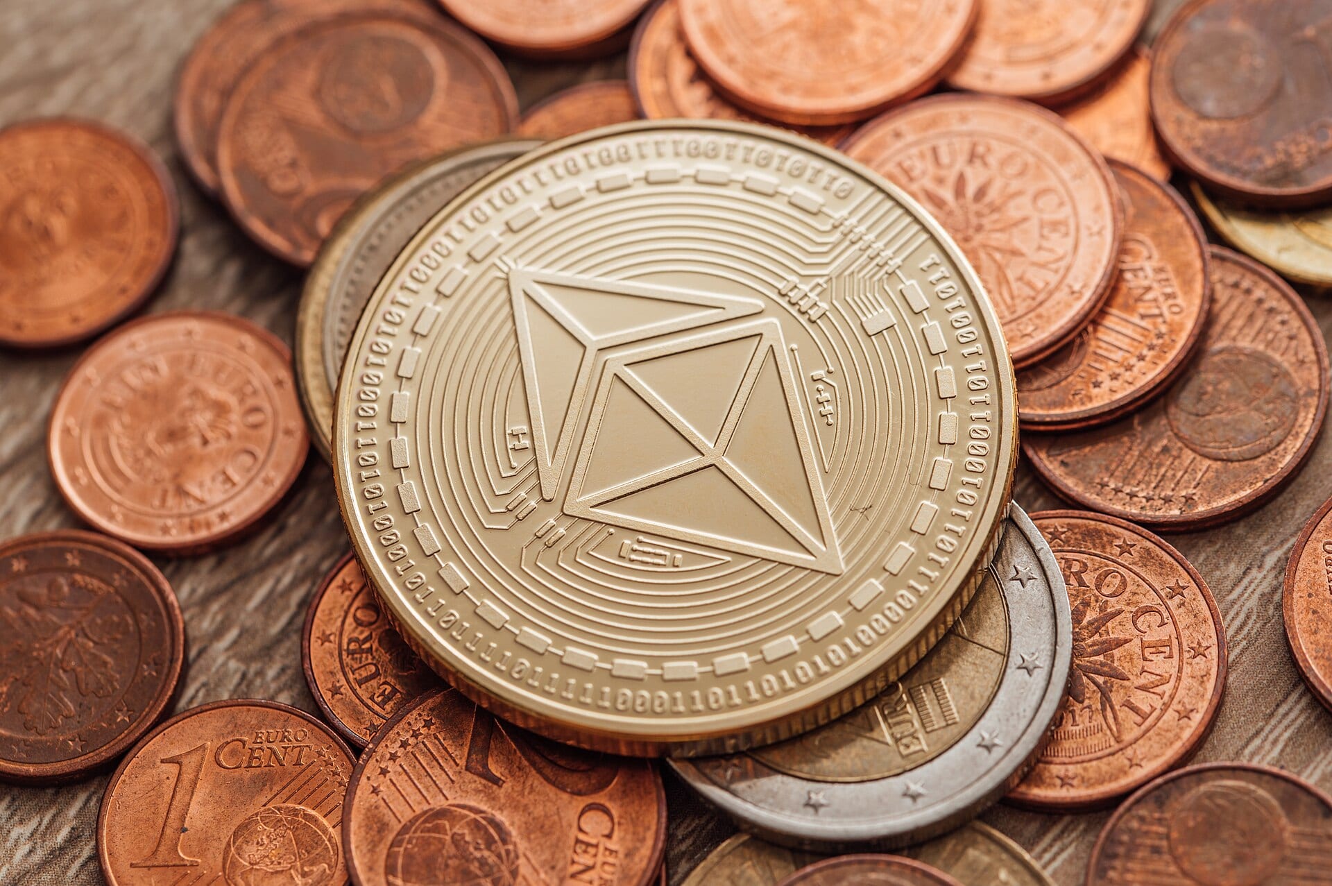 A gold coin bearing the Ethereum logo resting on a pile of euro cent coins.