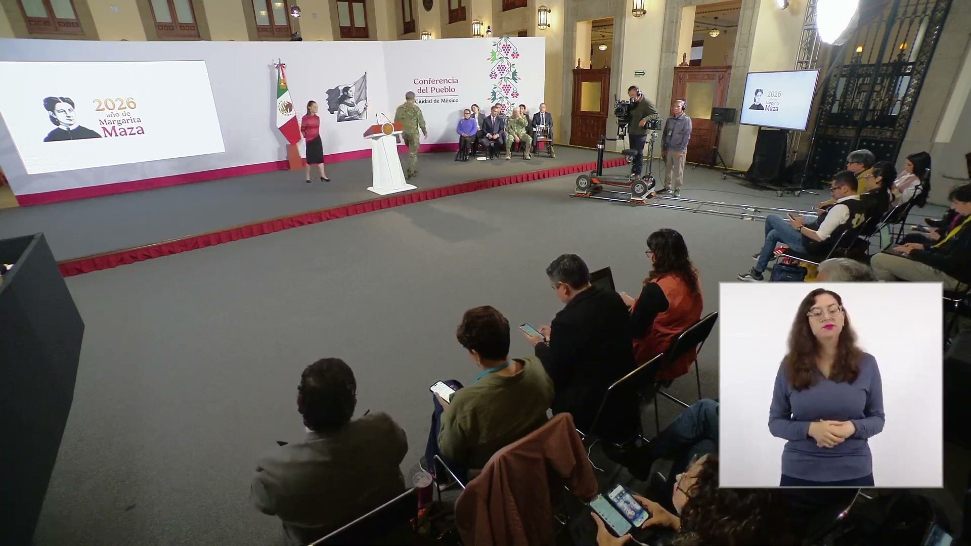 Vista general del salón de la conferencia matutina, con el estrado al fondo, la prensa sentada en primer plano y un intérprete de lengua de señas en un recuadro.