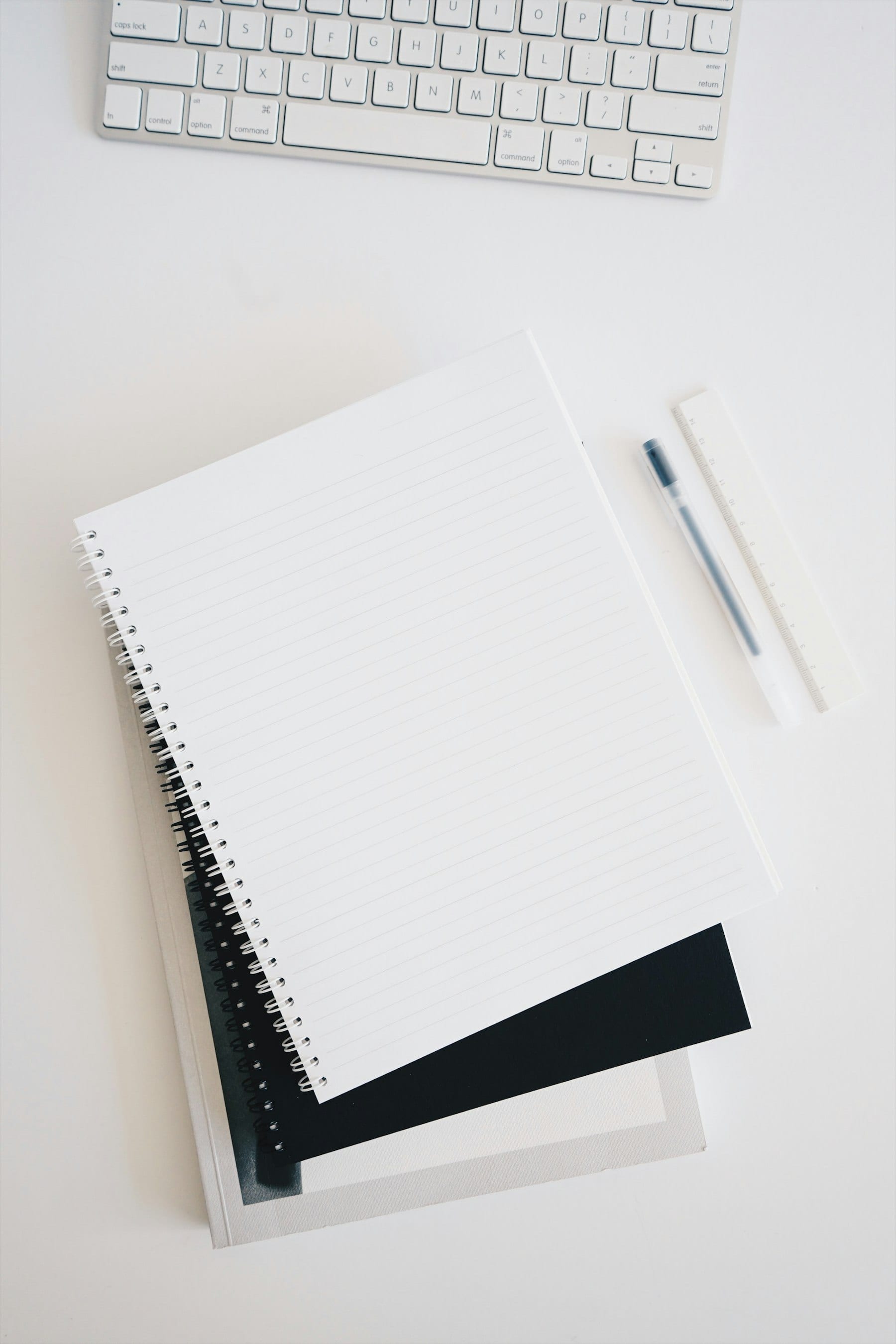 Libreta espiral en blanco sobre un escritorio, junto a un teclado y un bolígrafo.