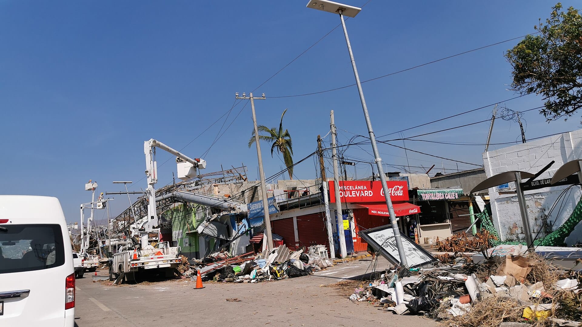 Calle de Acapulco con escombros, postes inclinados y cuadrillas con grúas reparando el cableado, días después del huracán Otis.