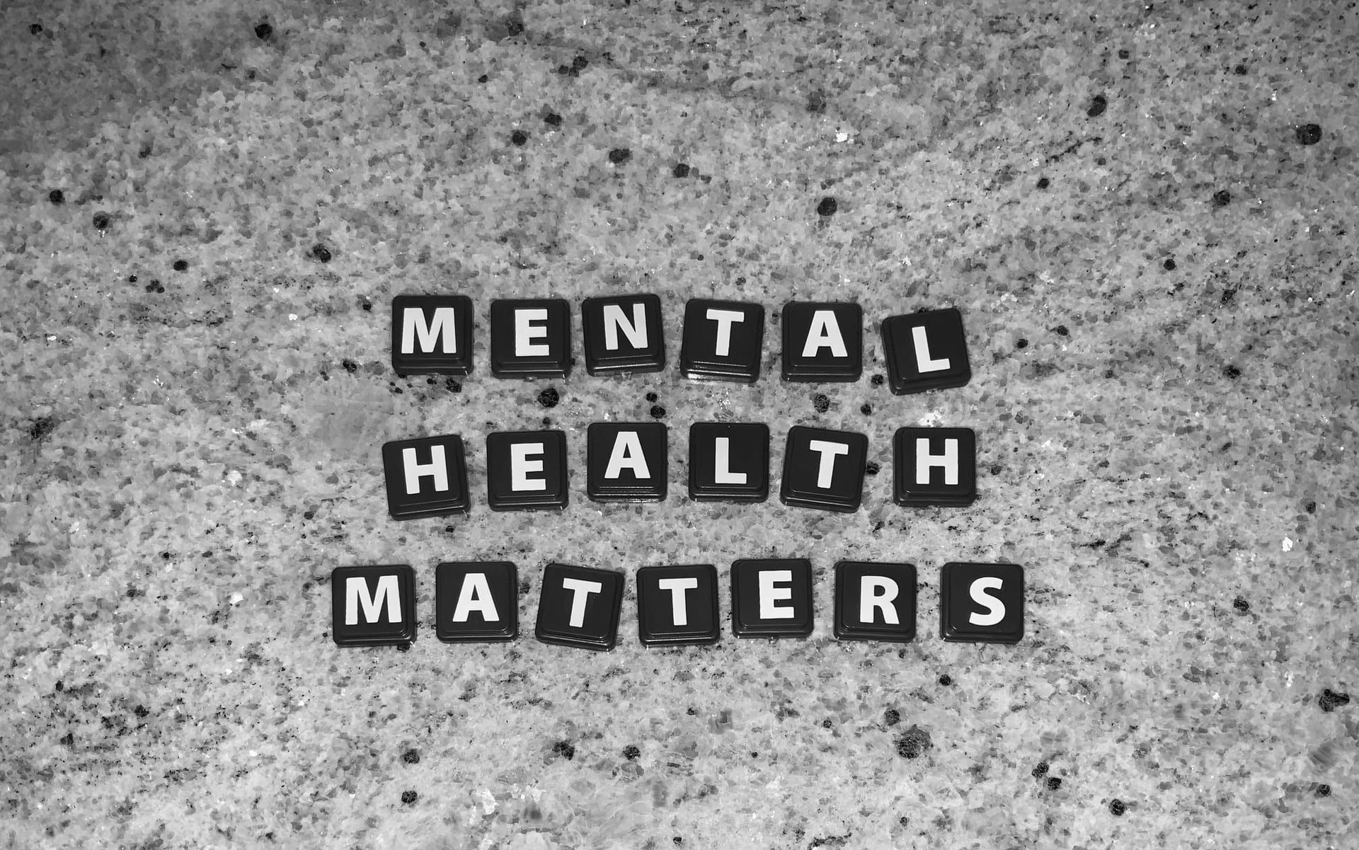 Fichas negras con letras blancas forman las palabras Mental Health Matters sobre una superficie de piedra moteada, en blanco y negro.
