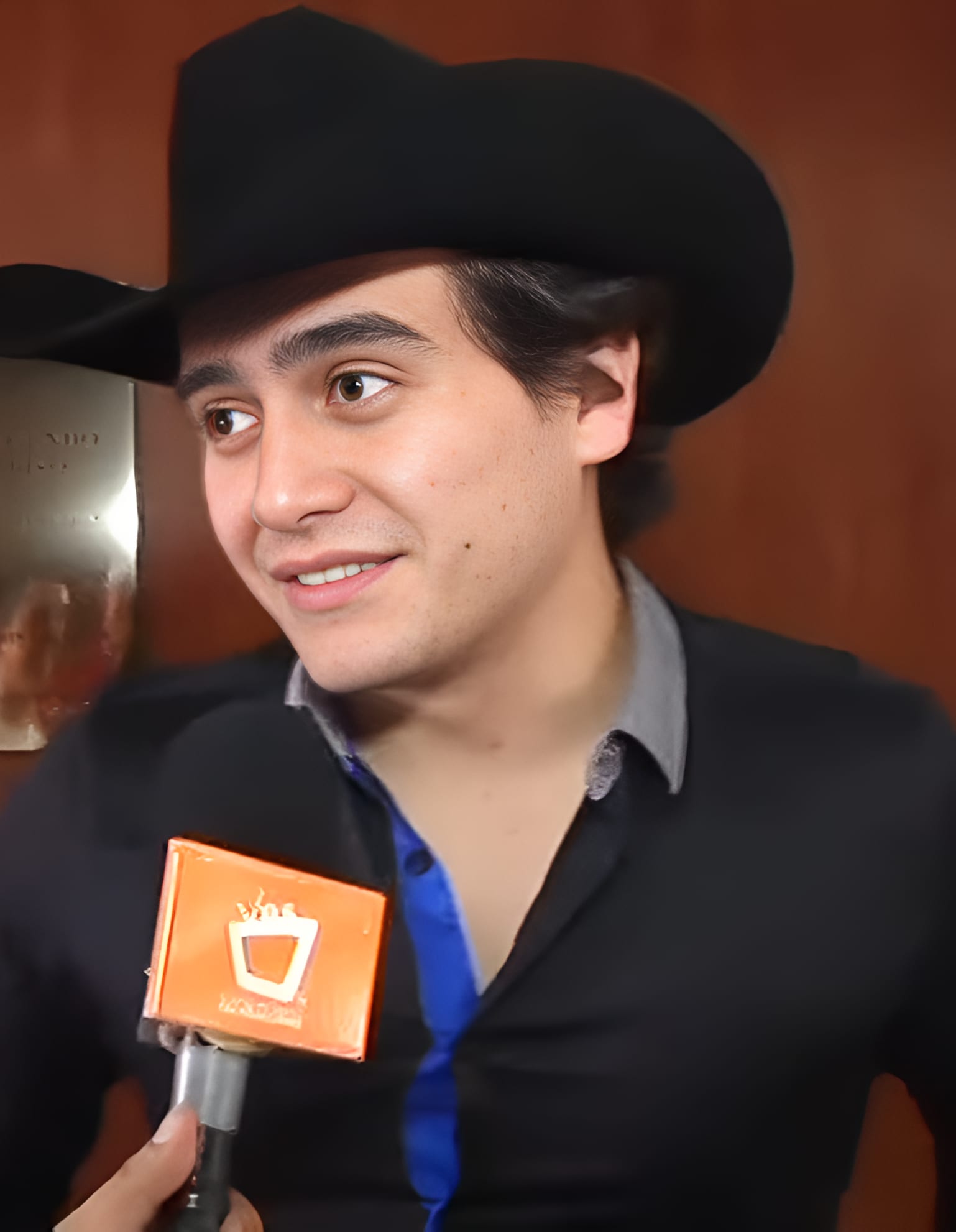 Julián Figueroa, con sombrero vaquero negro y camisa oscura, habla frente a un micrófono de entrevista.