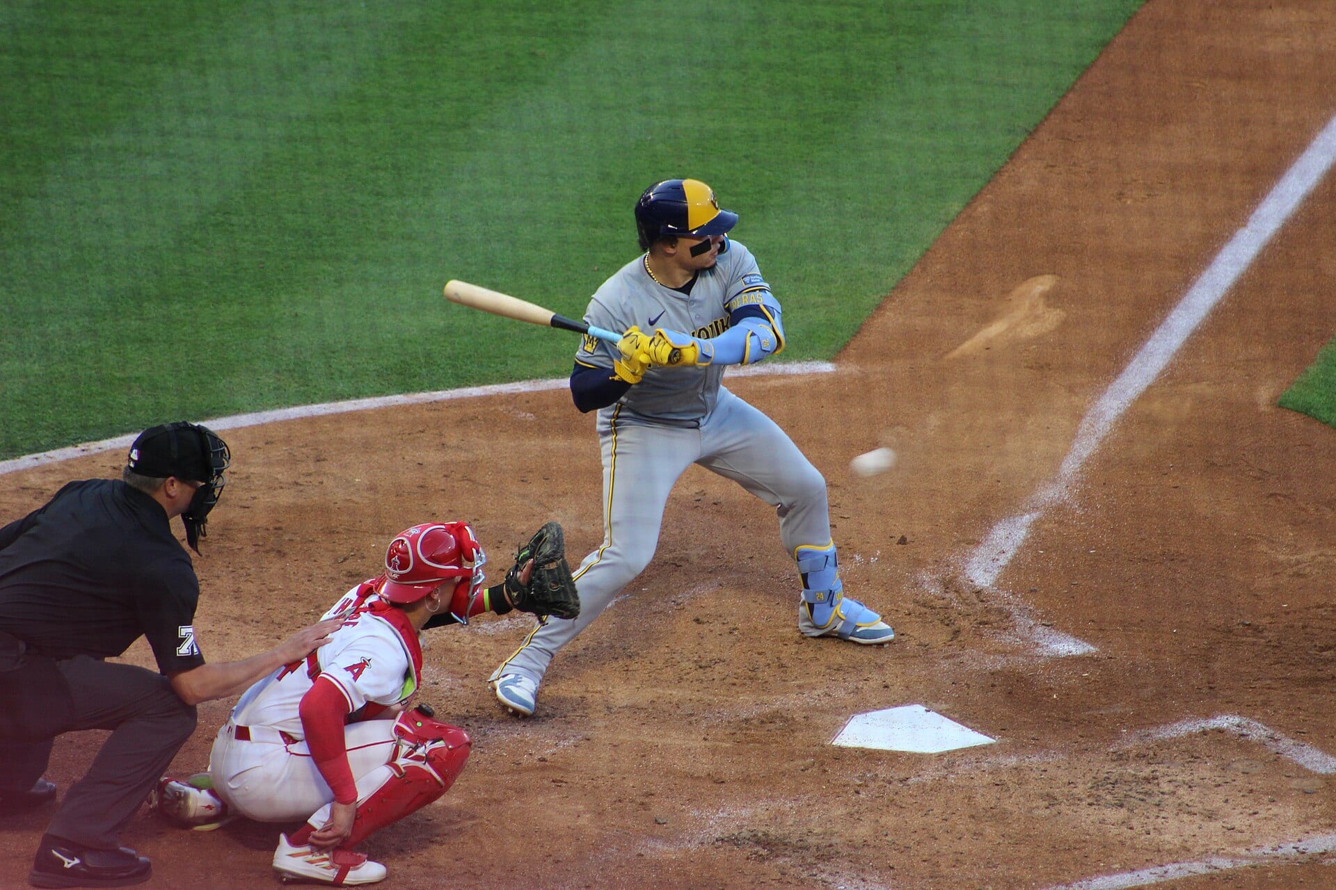 A Brewers batter in a blue and gold helmet waits for the pitch in front of an Angels catcher and an umpire.