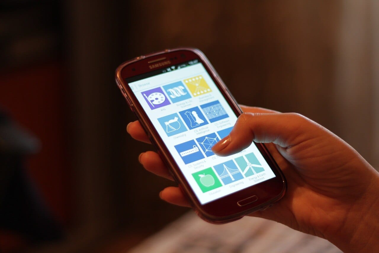 A hand holds a Samsung phone showing a screen of colorful app icons.