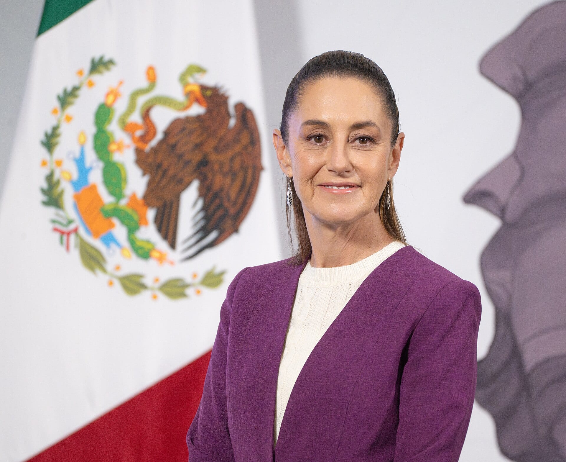 Retrato de la presidenta Claudia Sheinbaum con saco morado, frente a una bandera de México.