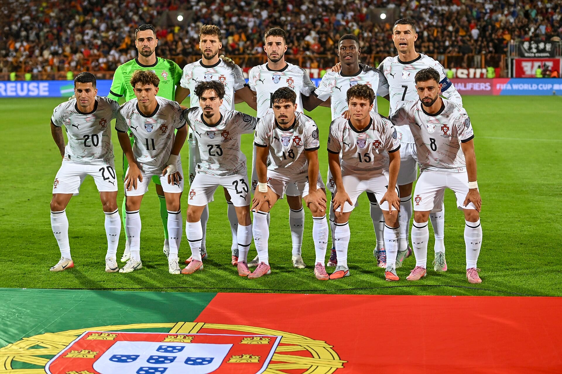 Once jugadores de Portugal con uniforme blanco posan en dos filas sobre el césped, con una bandera del país extendida frente a ellos.