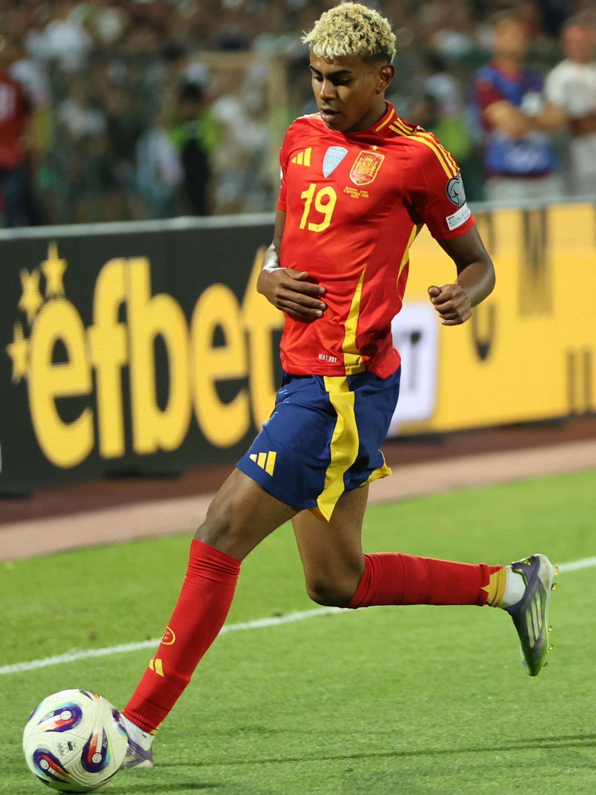 Lamine Yamal, con la camiseta roja de España, conduce el balón cerca de la banda en un partido de 2025.