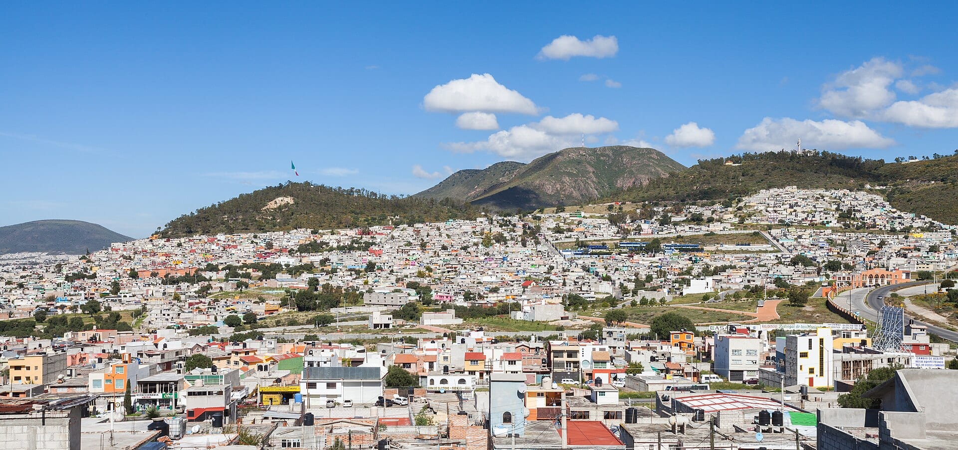 Casas de colores en una ladera de Pachuca, con cerros y un cielo azul con nubes al fondo.