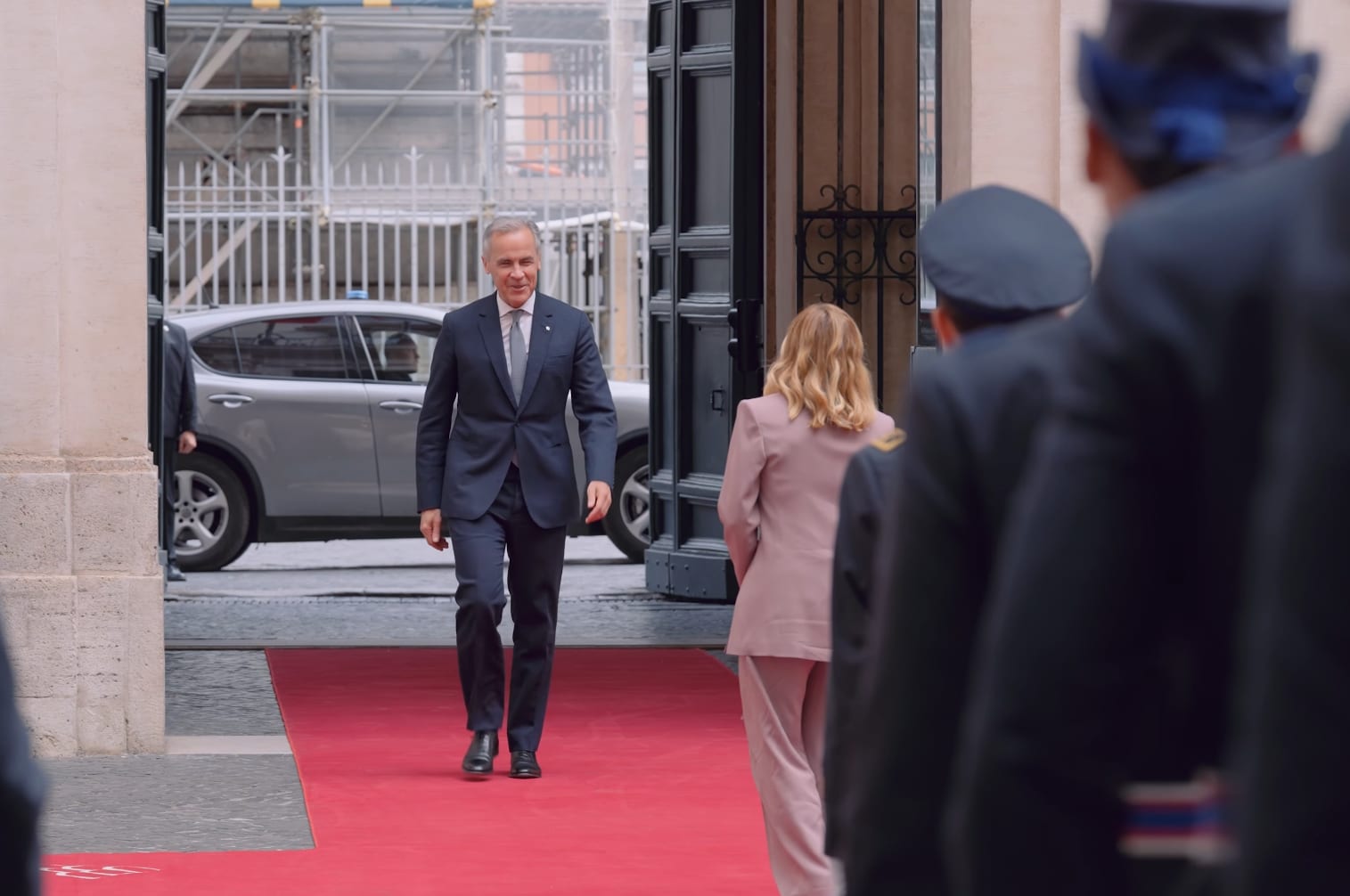 Canadian Prime Minister Mark Carney walks along a red carpet toward the entrance of a building in Rome, with an honor guard in the foreground.