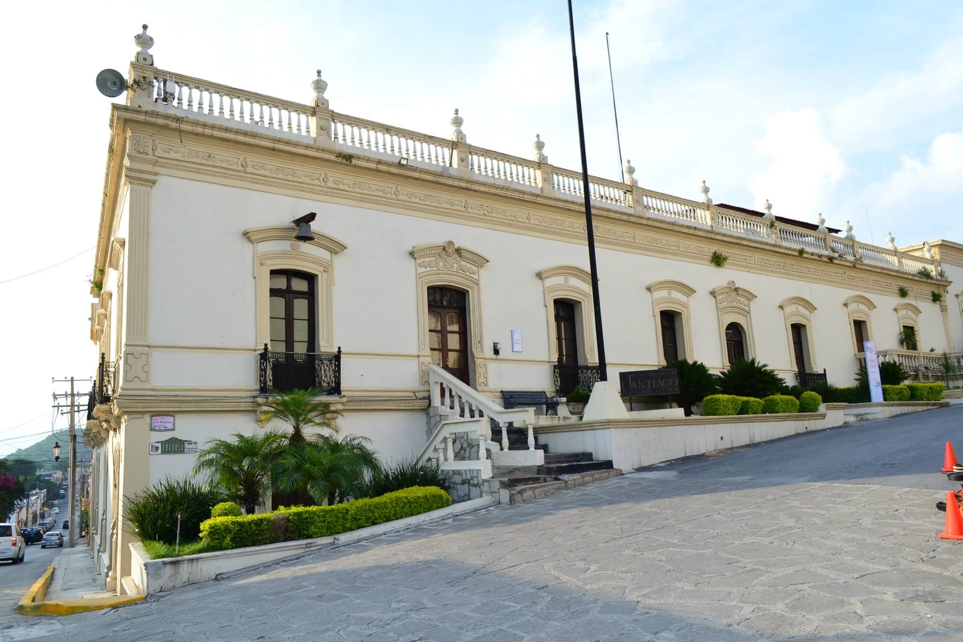 Fachada blanca con balaustrada del Palacio Municipal de Santiago, Nuevo León, en una calle empedrada en pendiente.