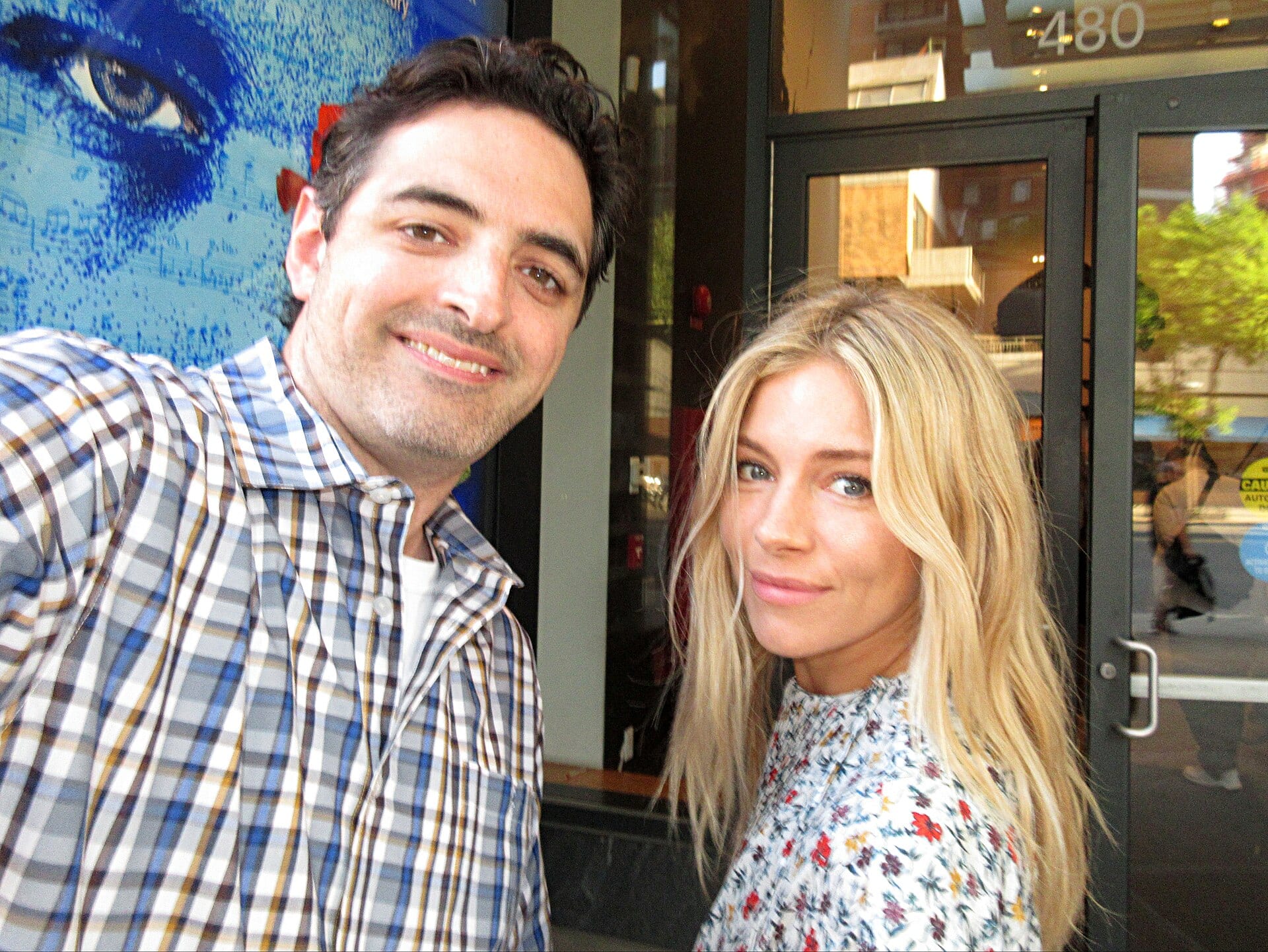 Sienna Miller sonríe de frente en una alfombra roja, con el pelo suelto y un vestido oscuro.
