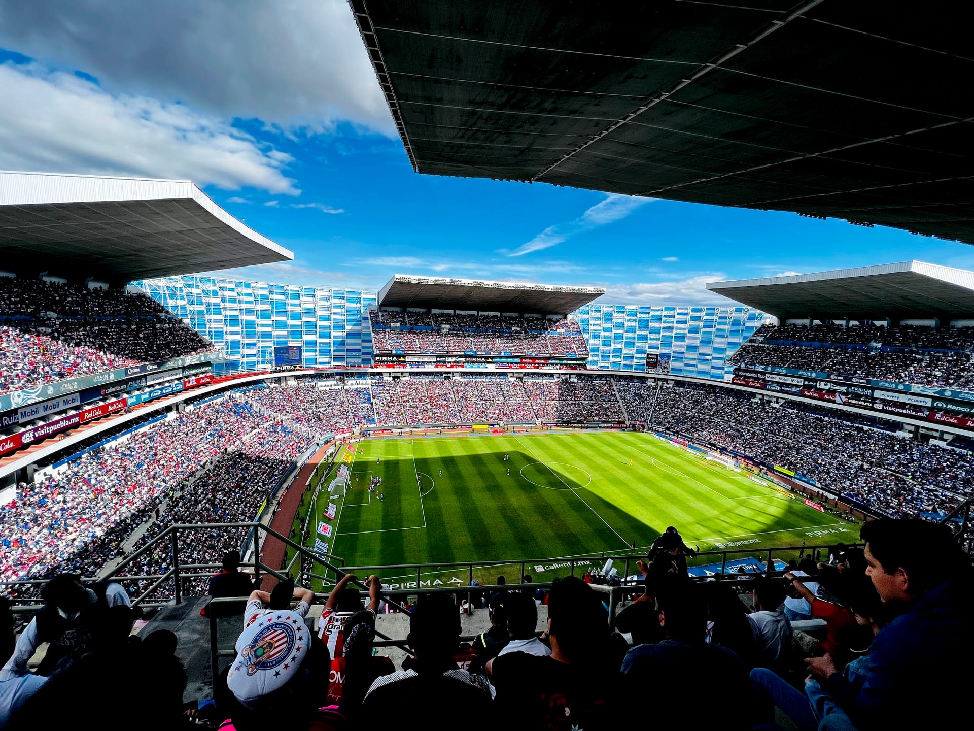 Vista desde lo alto de las gradas del Estadio Cuauhtémoc, con el campo iluminado a medias por la sombra de los techos.