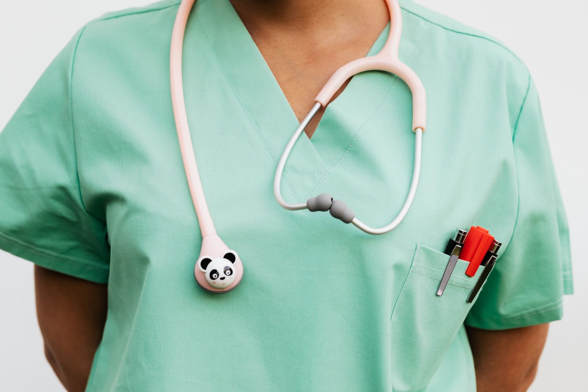 Torso de una persona con uniforme quirúrgico verde y un estetoscopio rosa con figura de panda colgado del cuello.