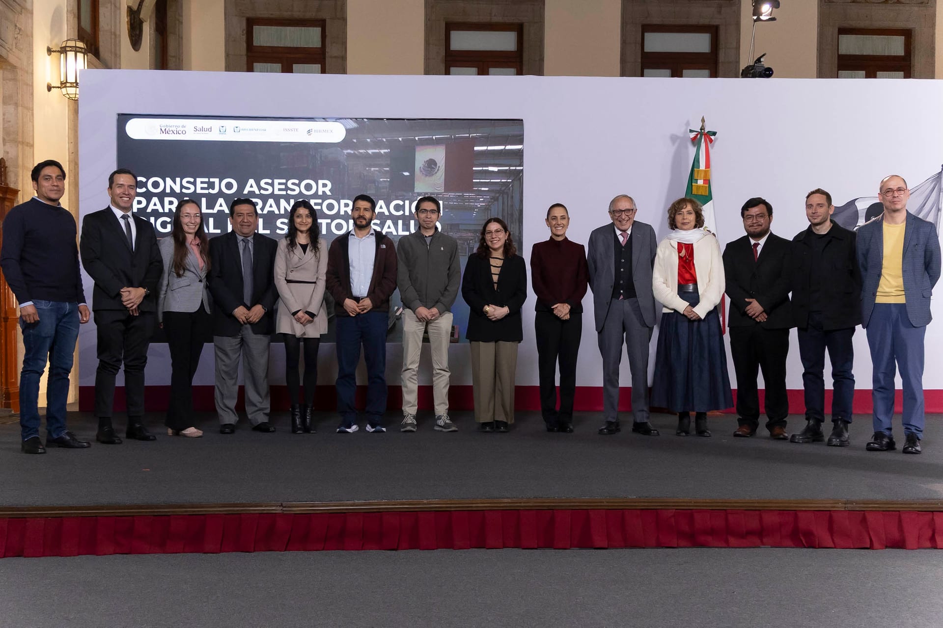 La presidenta Sheinbaum posa en Palacio Nacional con los integrantes del Consejo Asesor, de pie frente a una pantalla con el nombre del consejo.