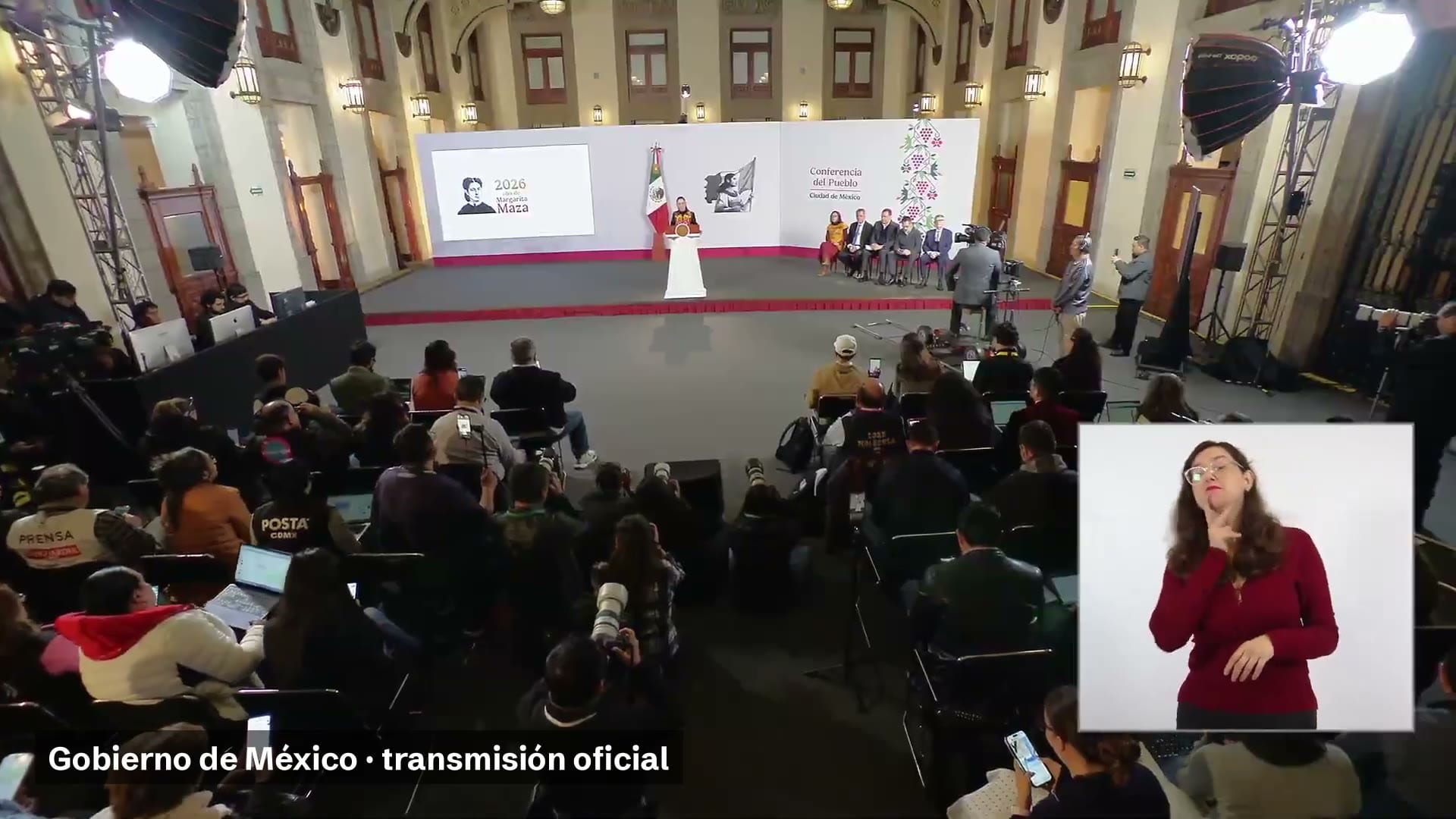 Salón de la conferencia matutina, con la presidenta de pie en el podio al fondo, reporteros en primer plano y una intérprete de lengua de señas en un recuadro.