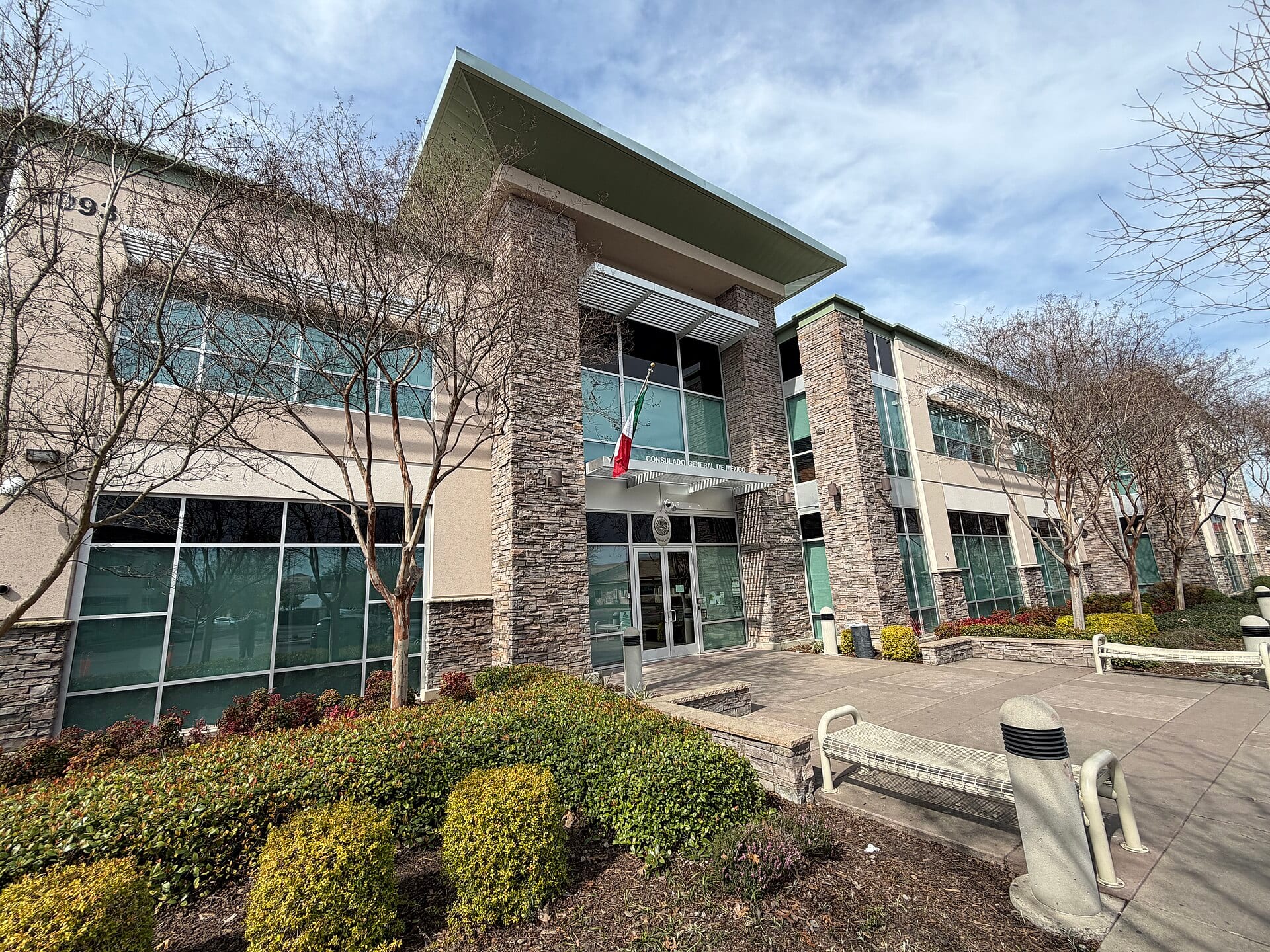 Entrada del Consulado General de México en Sacramento, un edificio de dos pisos con columnas de piedra y una bandera mexicana sobre la puerta.